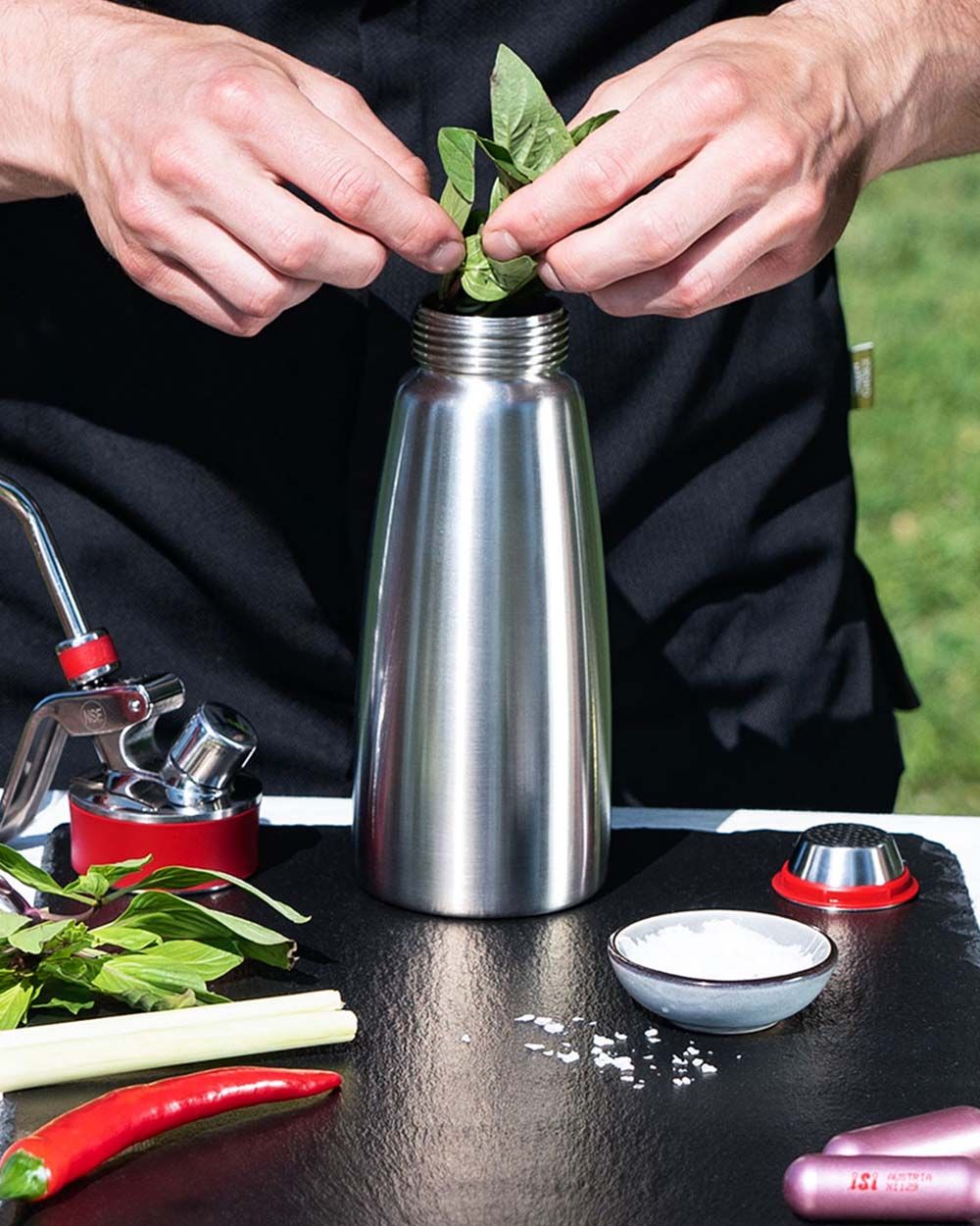 Jemand gibt Thai Basilikum in einen  iSi Gourmet Whip, um asiatisches Öl herzustellen. 