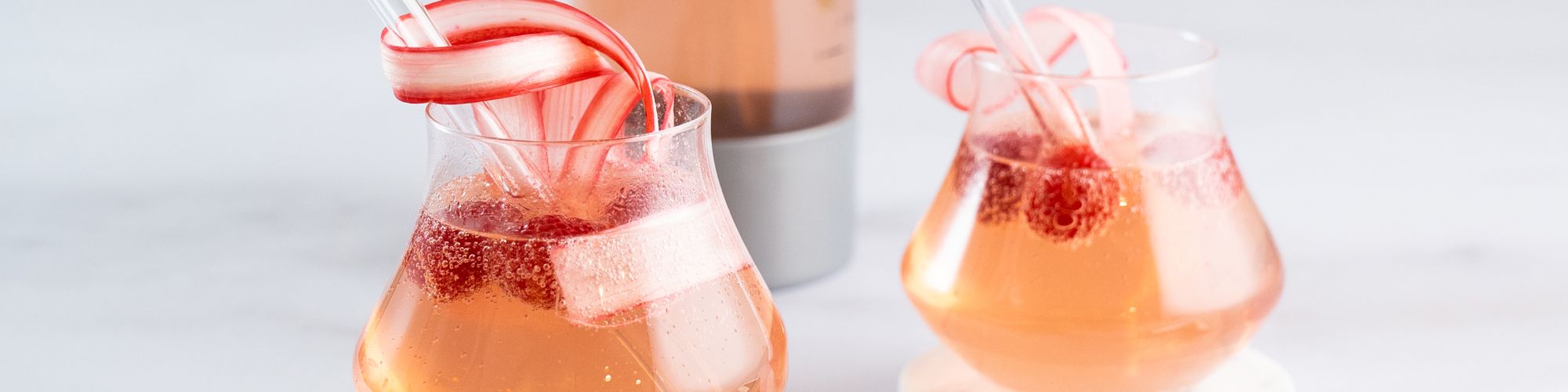 Zwei Gläser mit rosa sprudelndem Getränk, Himbeeren und dekorativen Apfelstreifen.