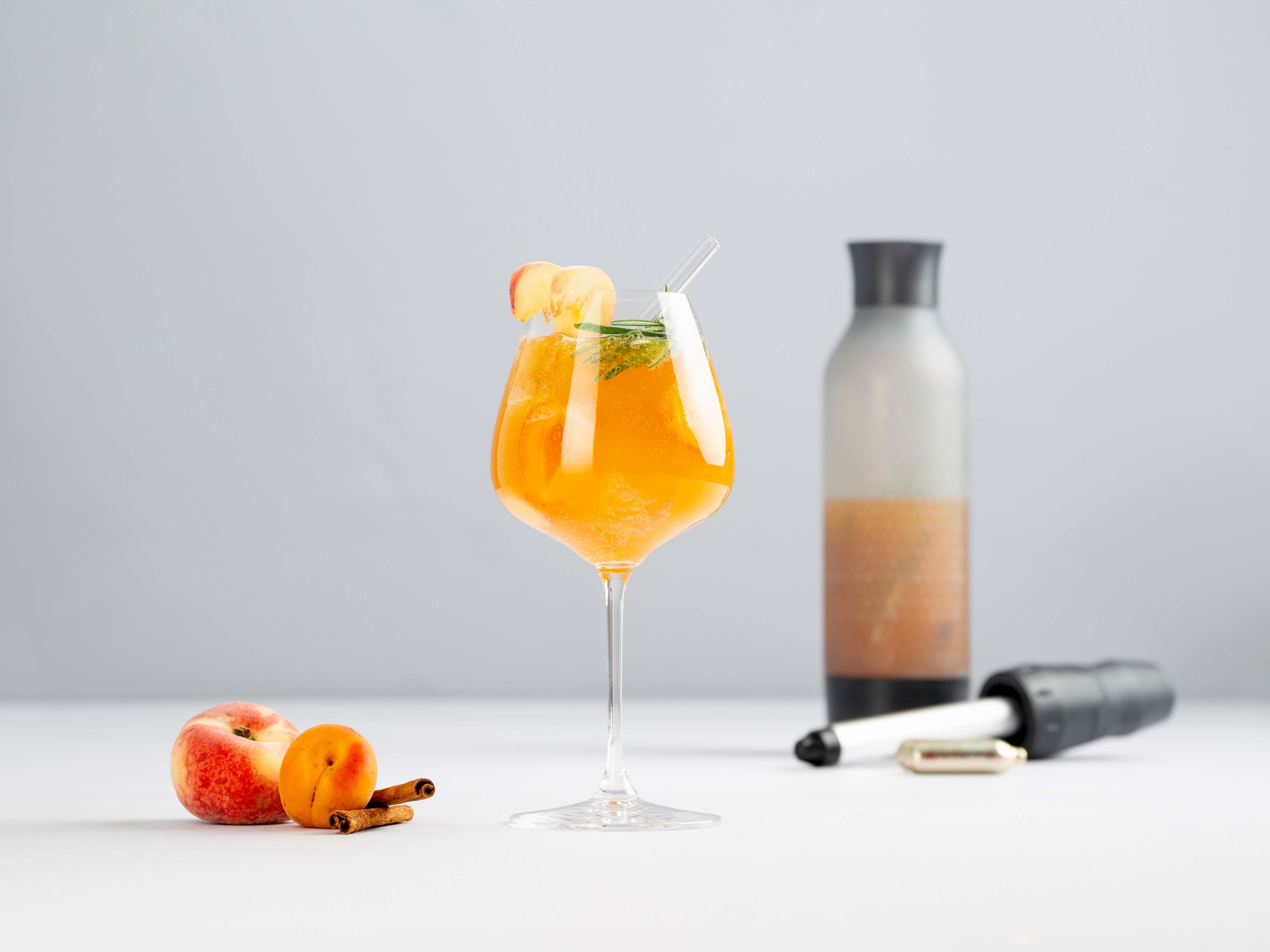 Ein Glas mit einem orangenen Getränk – Apricot Spritz – daneben Mandarinen und ein iSi Twist'n Sparkle. 
