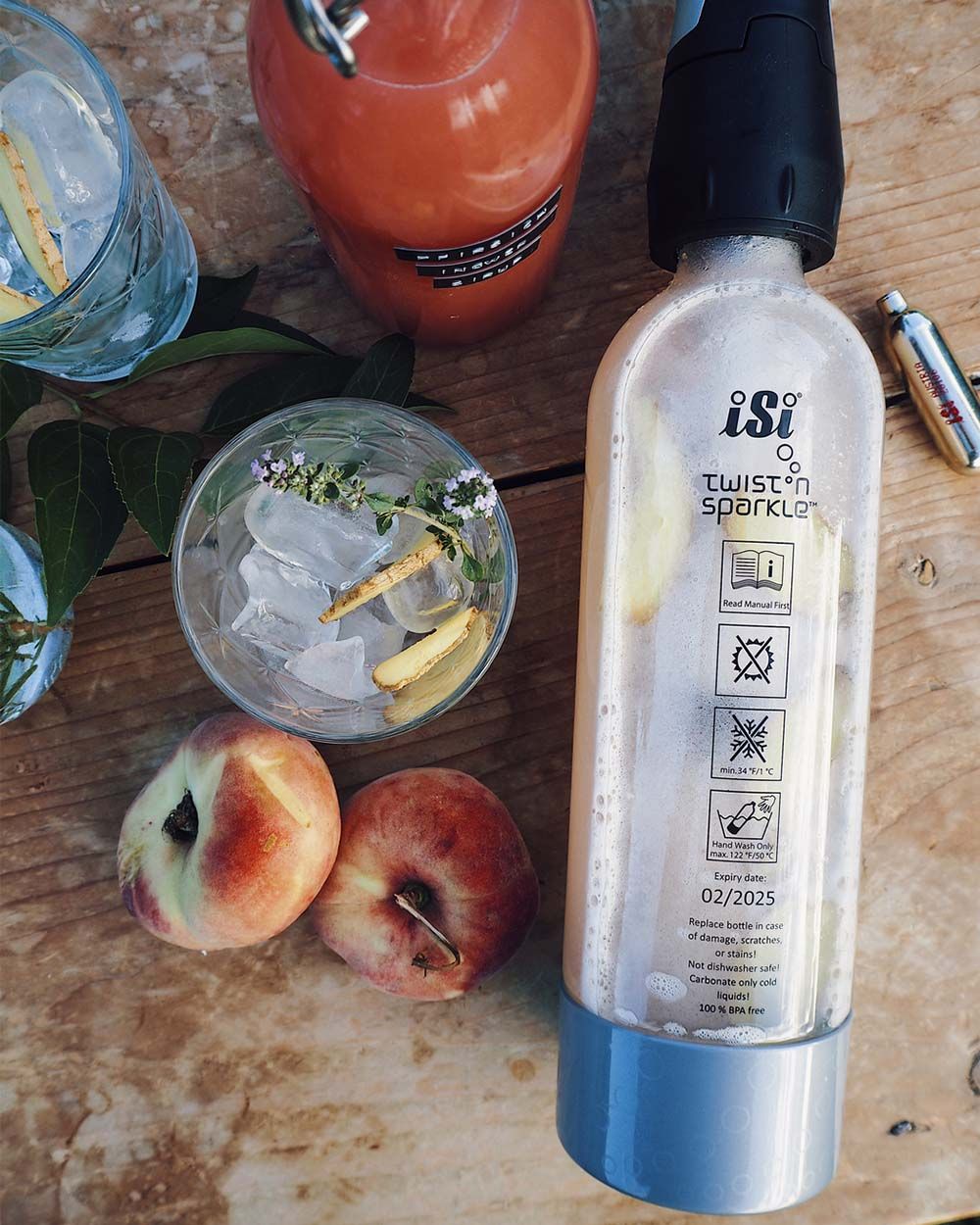 Ein iSi Twist'n'Sparkle Virtuoso, daneben ein Glas mit Eis und Pfirsiche. 