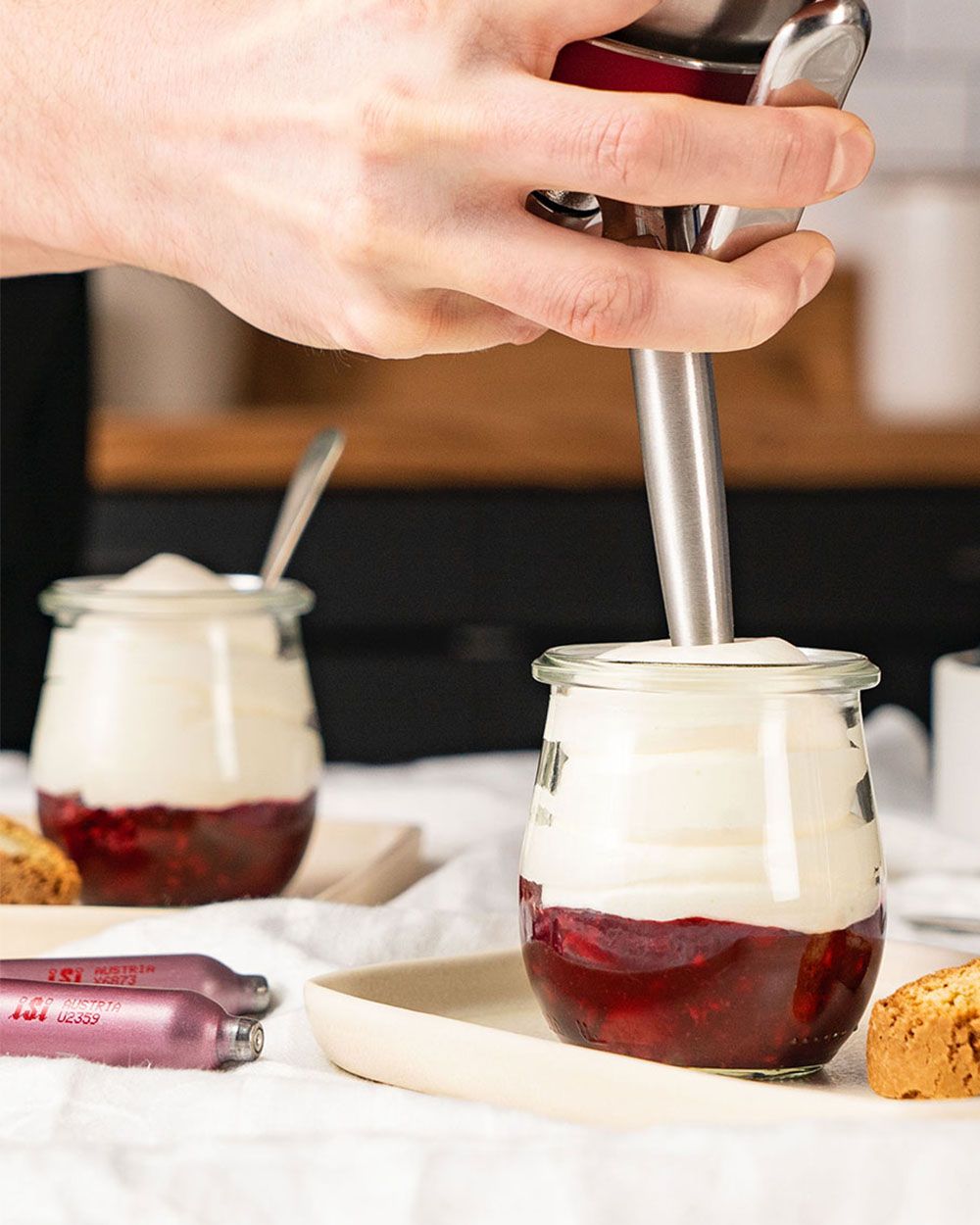 Jemand sprüht mit einem iSi Gourmet Whip Reispudding in zwei Gläser. 