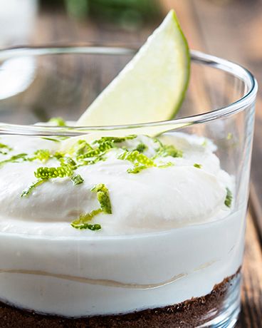 Ein Dessert im Glas mit Keksboden, cremiger weißer Schicht, Limettenabrieb und einer Limettenspalte als Garnitur.