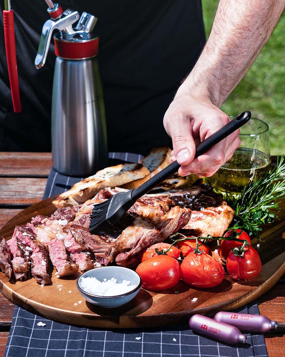 Jemand bestreicht Fleisch mit mediterranem Öl, daneben Gemüse, iSi Charge Kapseln und ein iSi Gourmet Whip. 