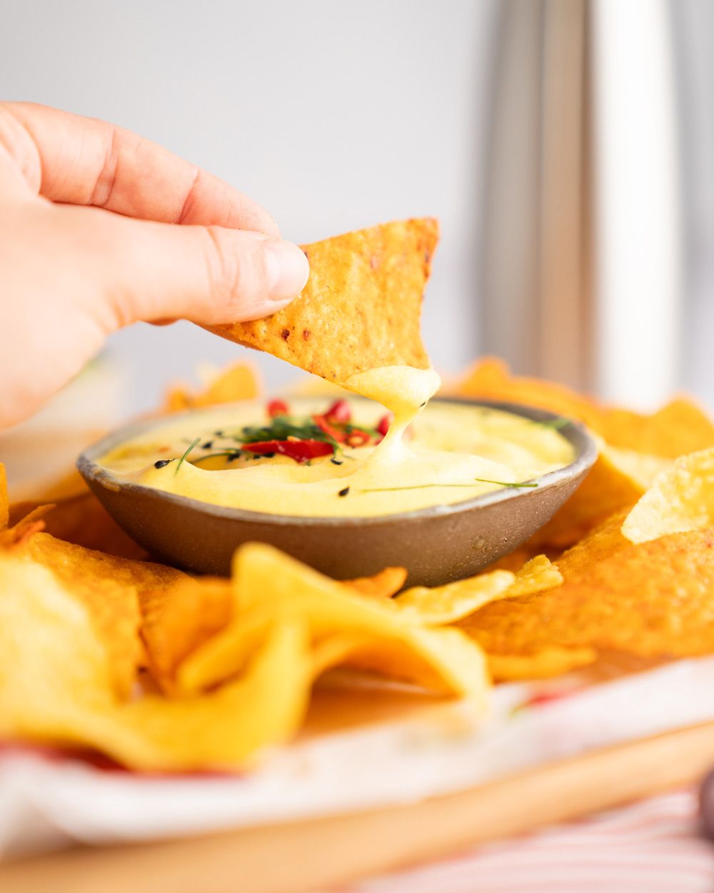 Jemand dippt ein Nacho in Käse-Espuma, daneben mehr Nachos. 