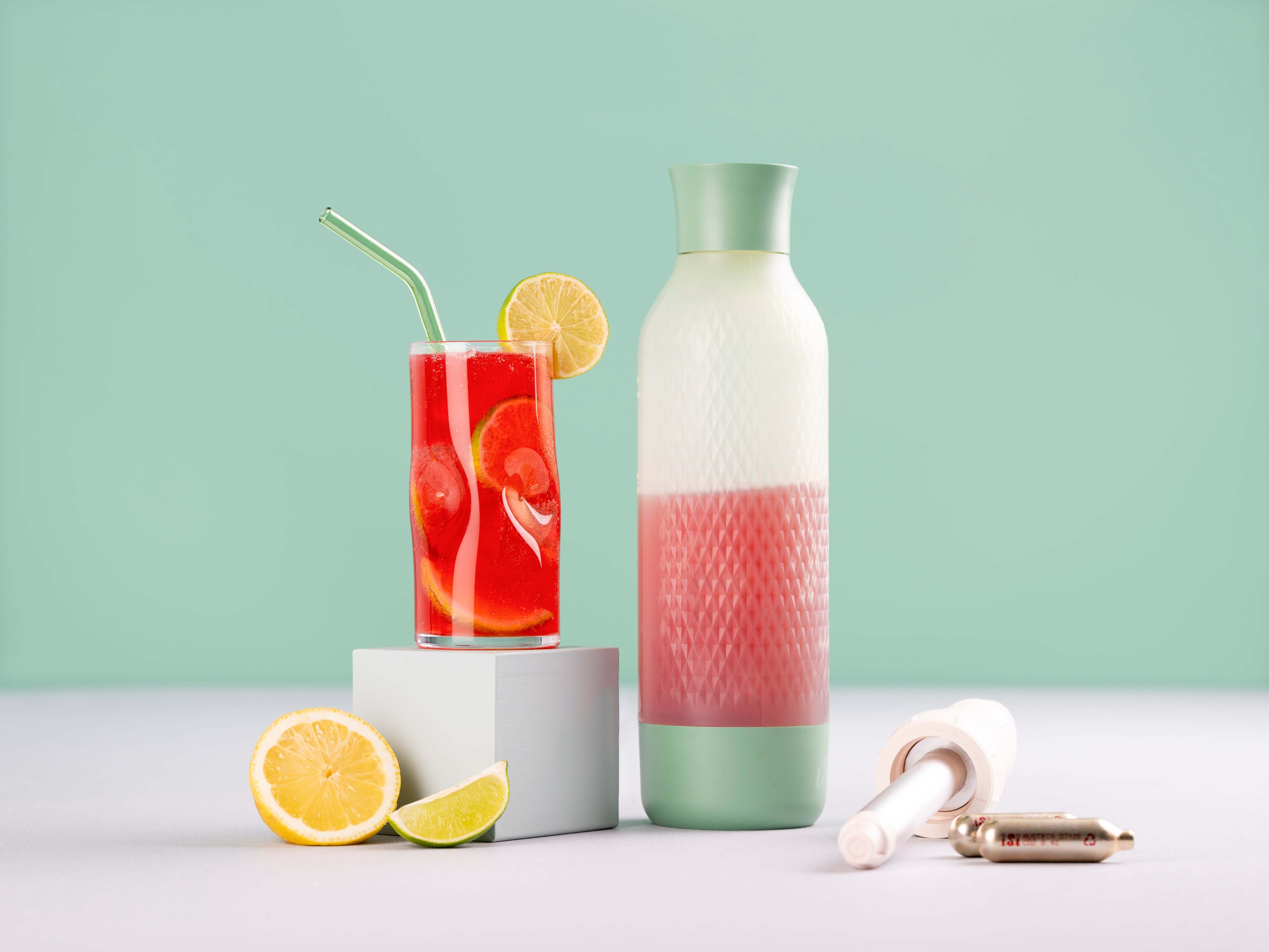 Ein Glas mit einem roten Getränk – Cranberry Ginger Lemonade – daneben eine Zitrone, ein iSi Twist'n Sparkle und iSi Charge Kapseln. 