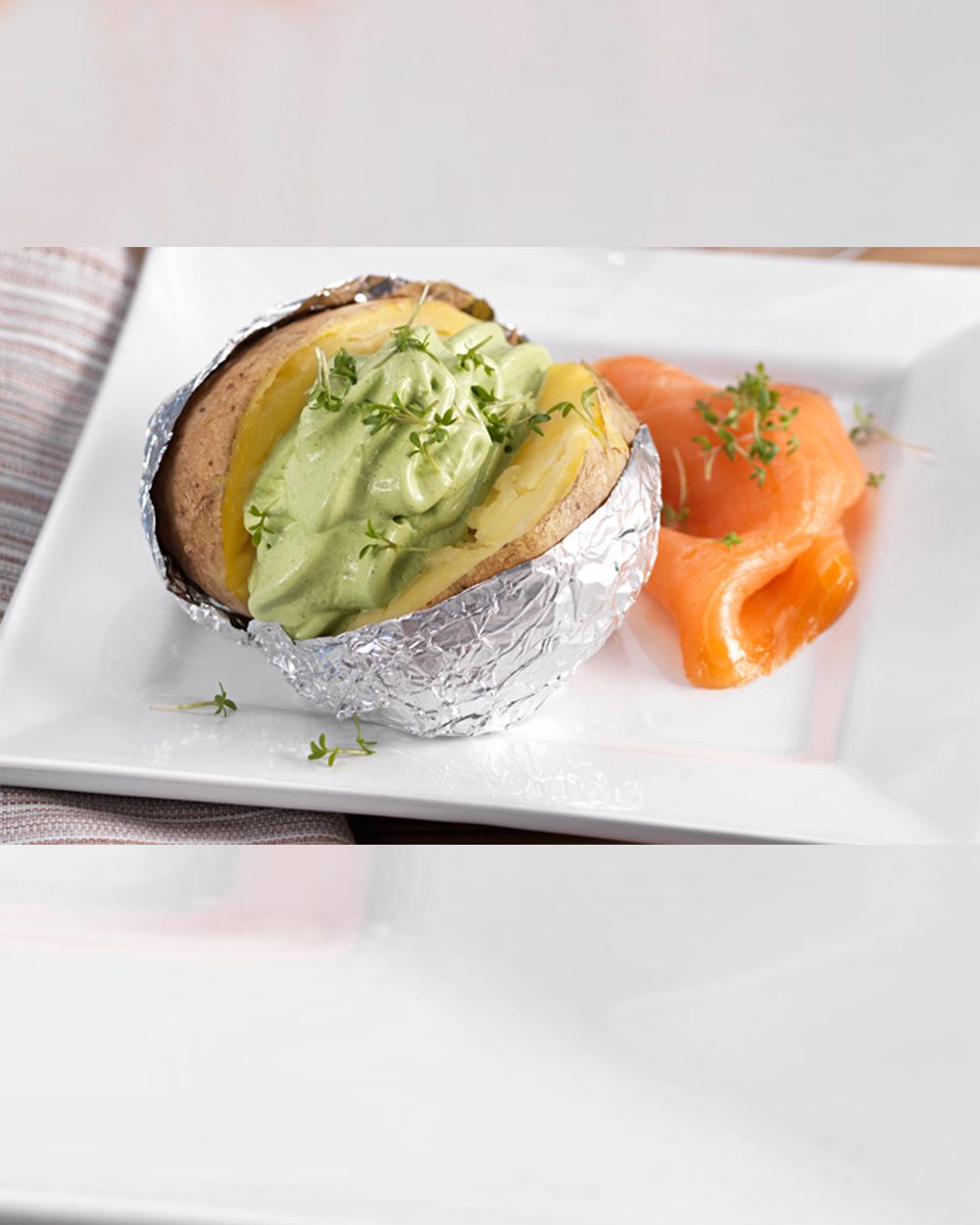 Eine Ofenkartoffel mit Avocado-Creme und Räucherlachs ist appetitlich auf einem weißen Teller angerichtet.