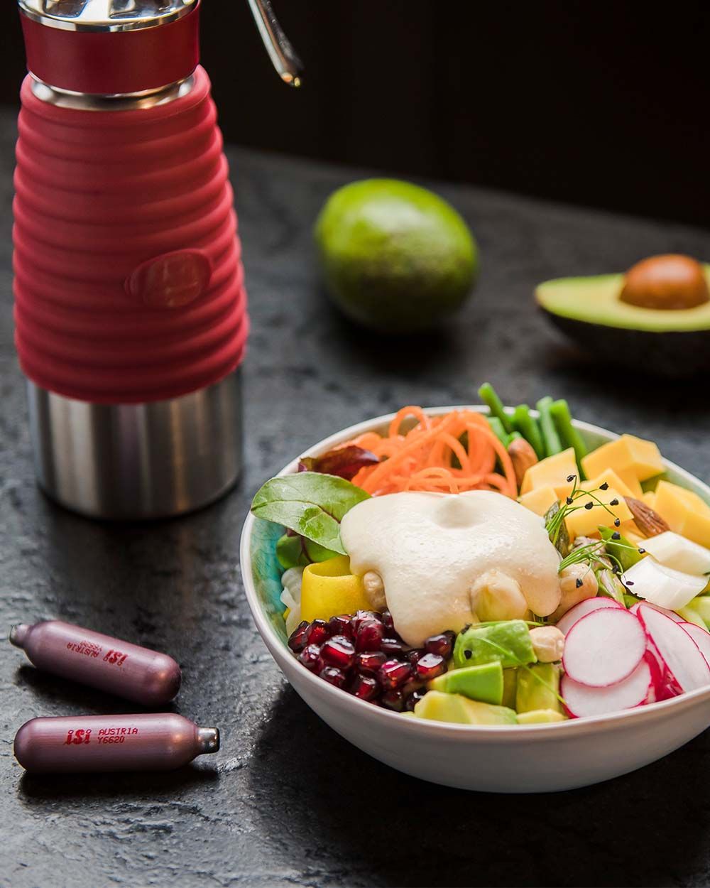 Eine Schüssel mit Gemüse und veganer Hollandaise Sauce, daneben iSi Charge Kapseln, ein iSi Gourmet Whip und Avocados. 