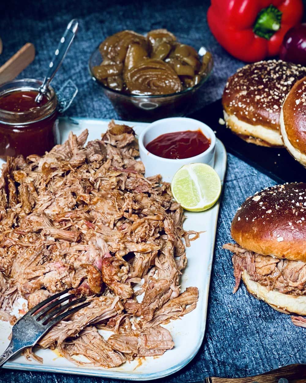 Ein Teller mit Pulled Pork, daneben Burger-Buns und Sauce. 