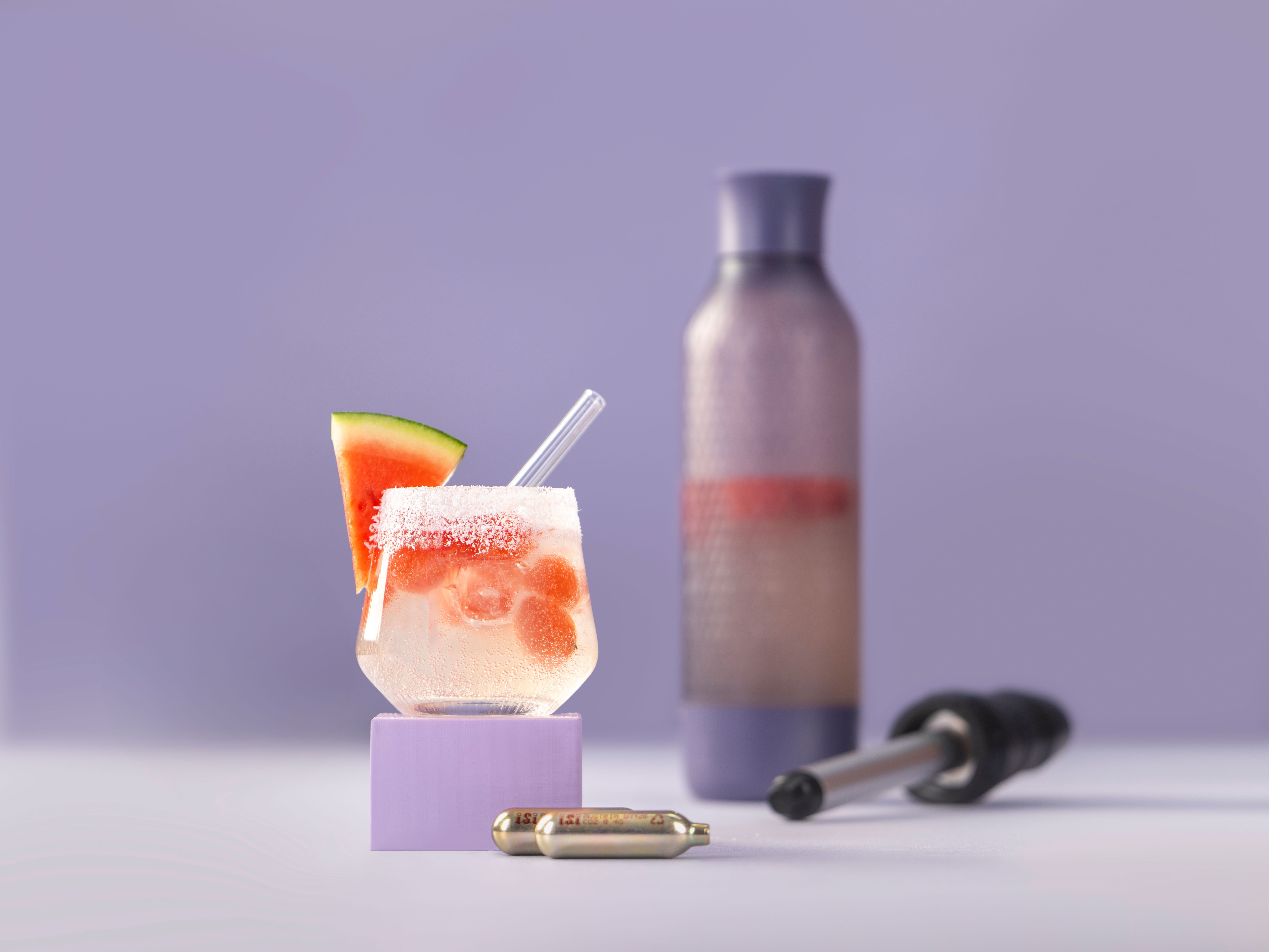 Ein Glas mit einem Getränk, Sparkling Cocomelon, daneben ein iSi Twist'n Sparkle und iSi Charge Kapseln.