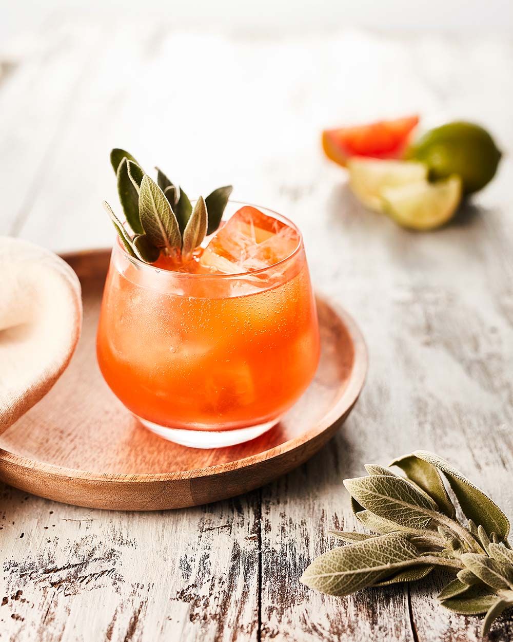 Ein Glas mit einem orangenen Getränk, im Hintergrund Limetten. 