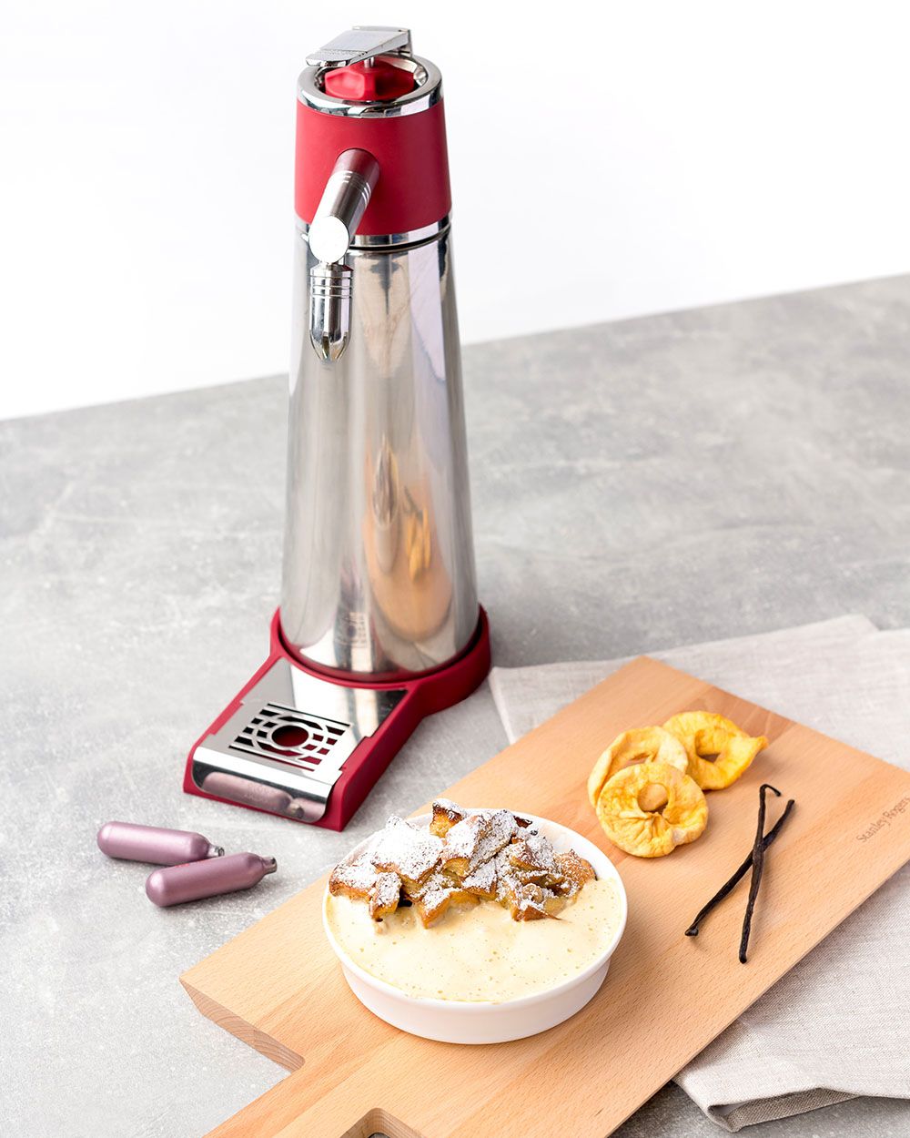 Ein Brett mit Kaiserschmarren und Vanillesauce, daneben Apfelringe, Vanilleschoten und iSi Charge Kapseln.  Im Hintergrund ein iSi Magic Texturiser.