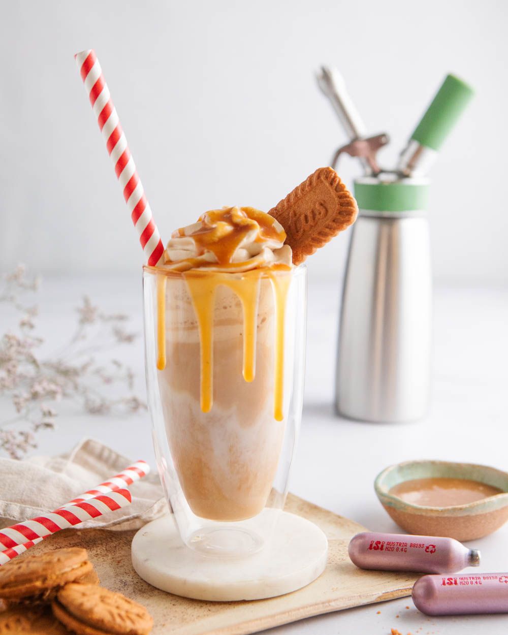 Ein Glas mit einem Lotus Cream Latte, davor zwei iSi Charge Kapseln, im Hintergrund ein iSi Creative Whip. 