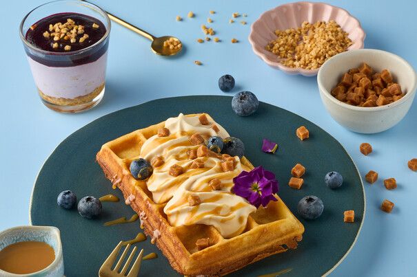 Ein Teller mit einer Waffel mit Toffee Sahne, daneben Müsli und Beeren. 