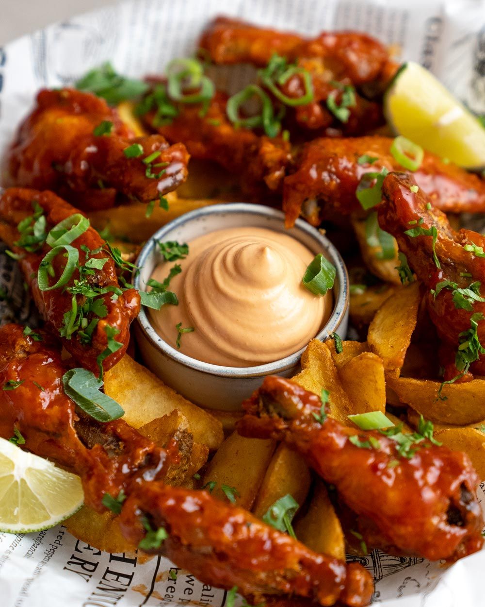 Auf dem Bild sieht man Chicken Wings mit Kartoffelspalten, Zitronenspalten und einem Dip in der Mitte.