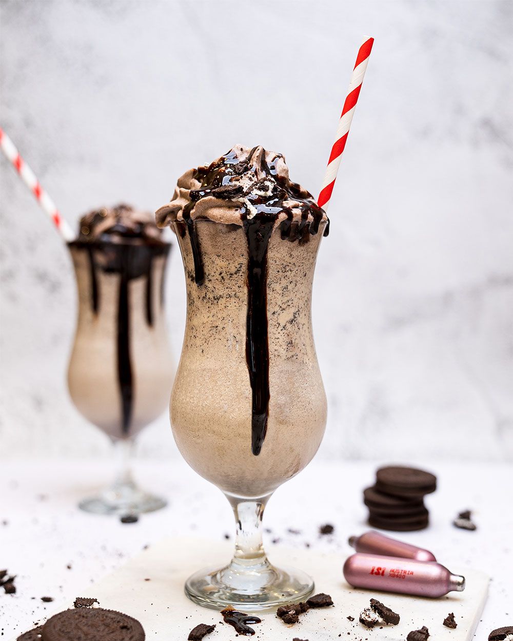 Zwei Gläser mit Oreo Cafe Latte, daneben iSi Charge Kapseln und Oreo Kekse. 