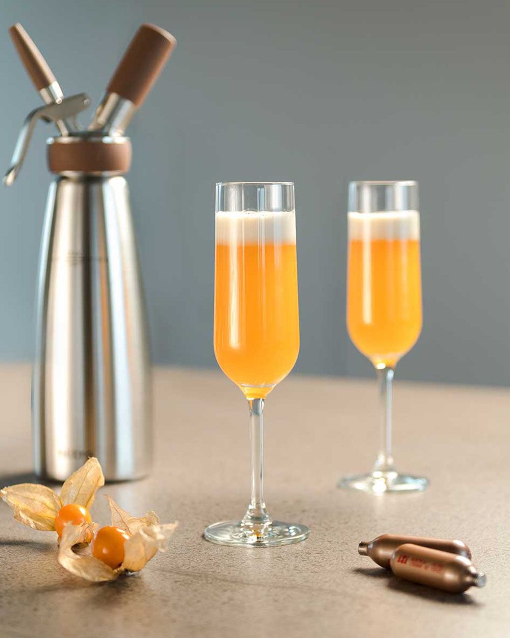 Zwei Gläser Nitro Bellini, daneben iSi Charge Kapseln und ein iSi Nitro. 