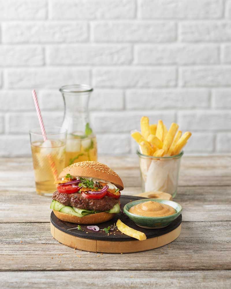 Ein Teller mit einem Burger und einer Schale mit Dipsauce, daneben Pommes und Limonade. 