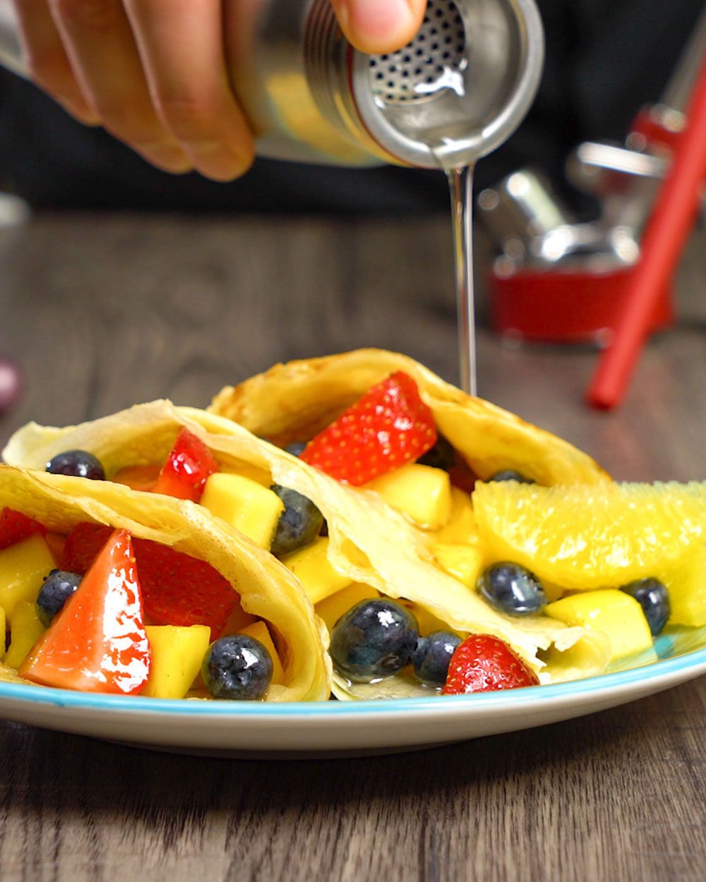 Jemand gießt aus einem iSi Gourmet Whip Vanillesirup auf Palatschinken mit Obst gefüllt. 