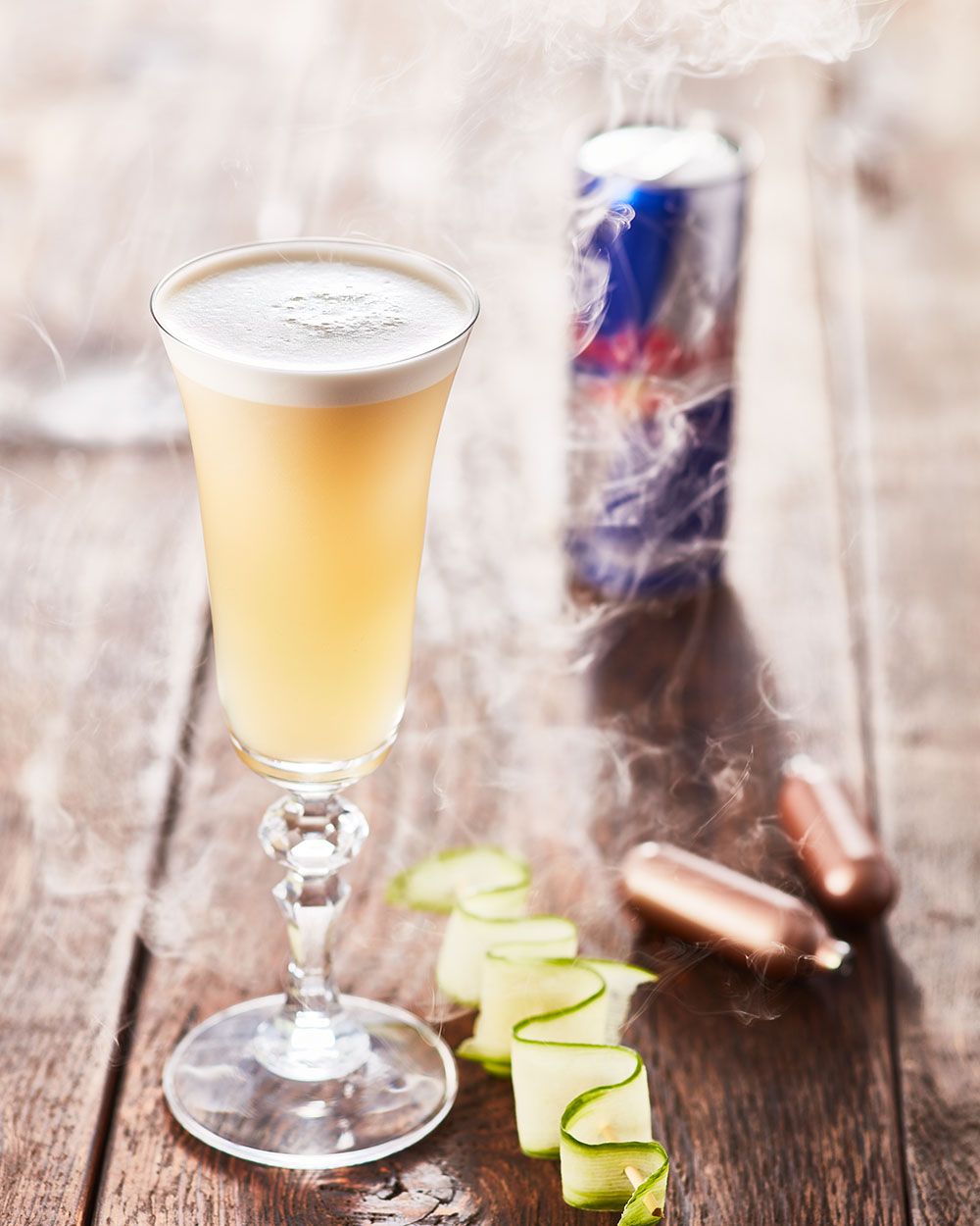 Ein Glas mit Red Bull Ginger Ale, daneben eine Gurkenspirale, iSi Charge Kapseln und eine Red Bull Dose. 