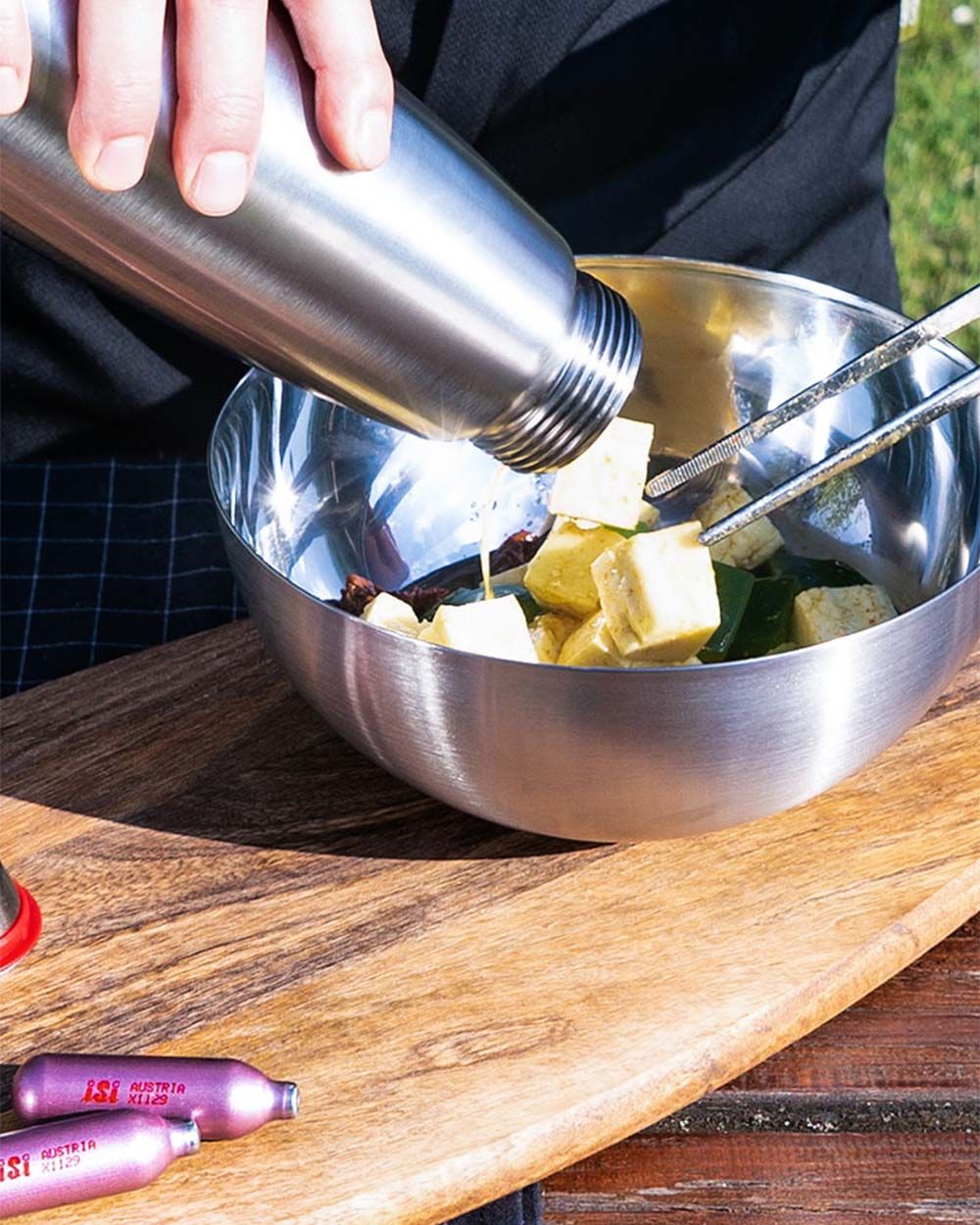 Jemand gießt Marinade aus einer iSi Gourmet Whip in eine Schüssel mit Halloumi, daneben zwei iSi Charge Kapseln.