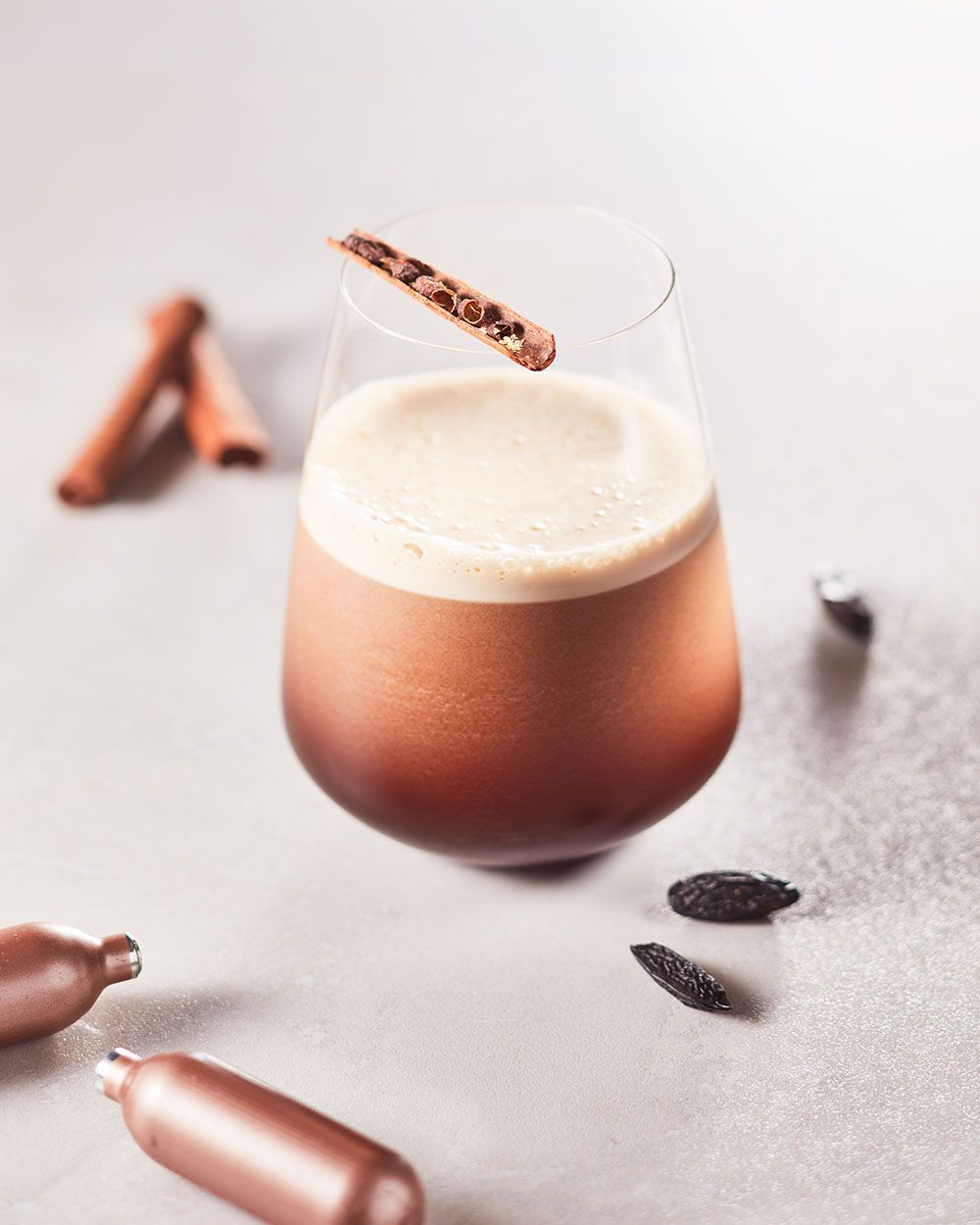 Ein Glas mit Nitro Zimt-Pfeffer Getränk, daneben iSi Charge Kapseln und Gewürze. 