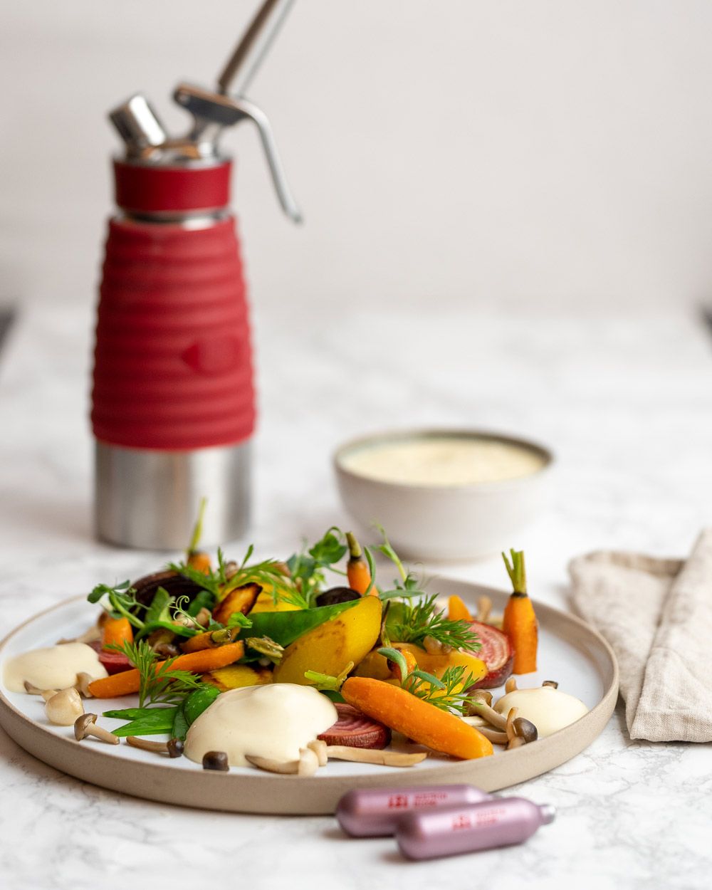 Ein Teller mit Gemüse und Polentaschaum, daneben iSi Charge Kapseln und im Hintergrund ein iSi Gourmet Whip.