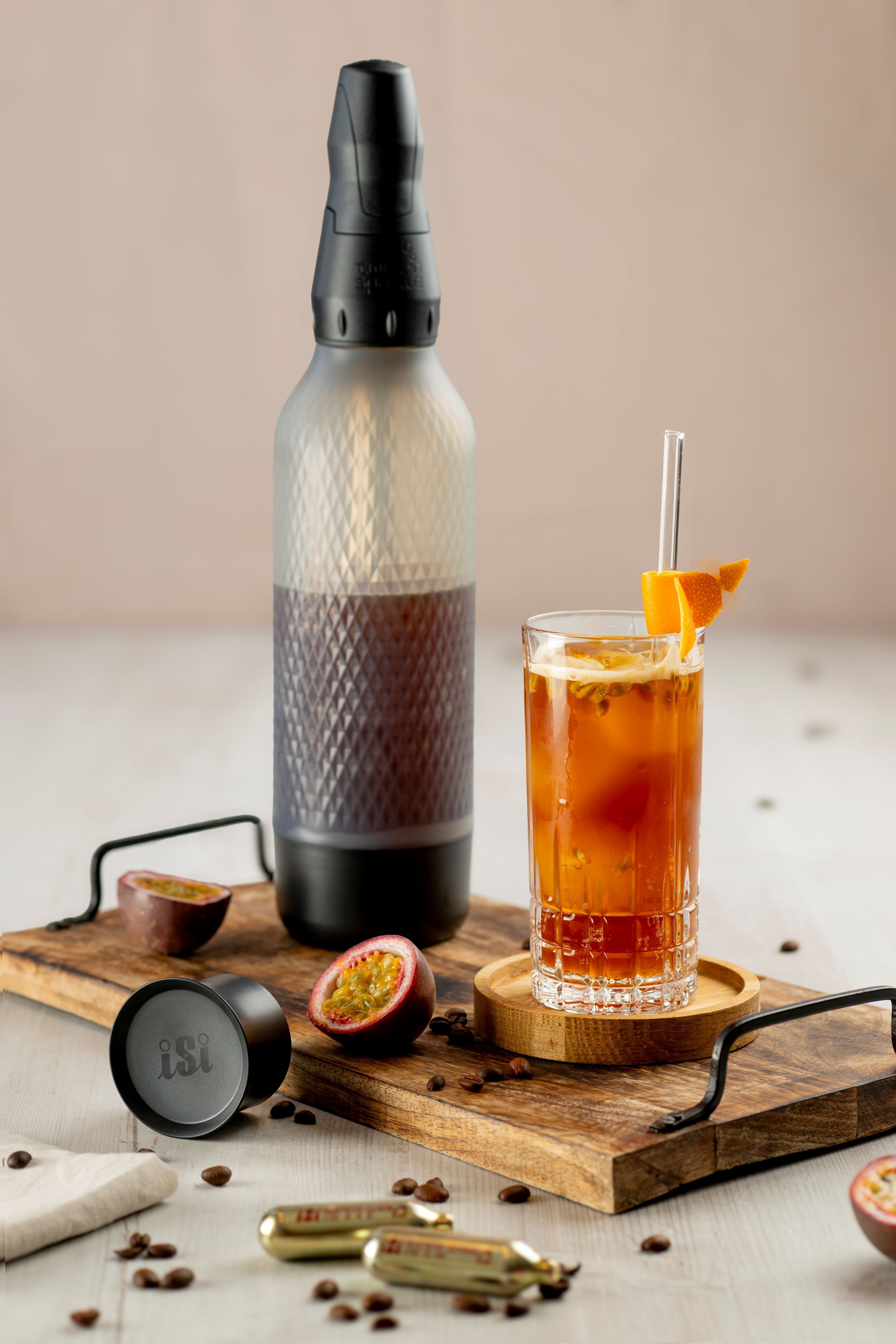 Ein Glas mit Sparkling Coffee, daneben ein iSi Twist'n Sparkle, iSi Charge Kapseln und Passionsfrüchte.
