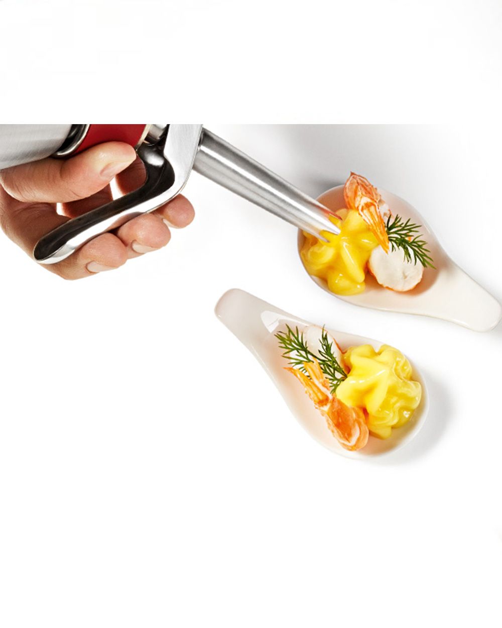 Jemand sprüht mit einem iSi Creative Whip Safran-Schaum in eine Schüssel, daneben eine bereits gefüllte Schüssel. 