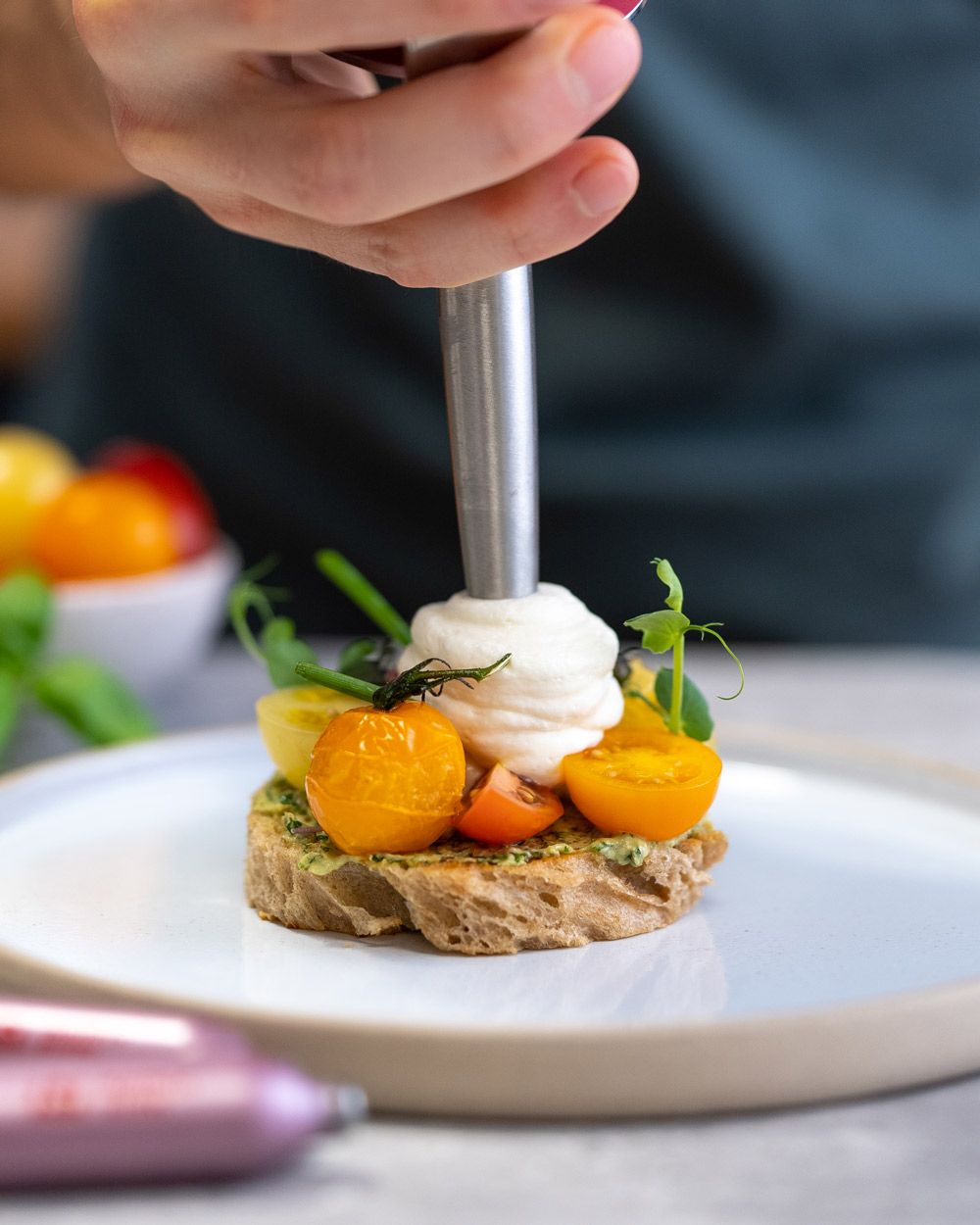 Jemand sprüht Burrata Espuma auf ein Tomaten-Tarte.