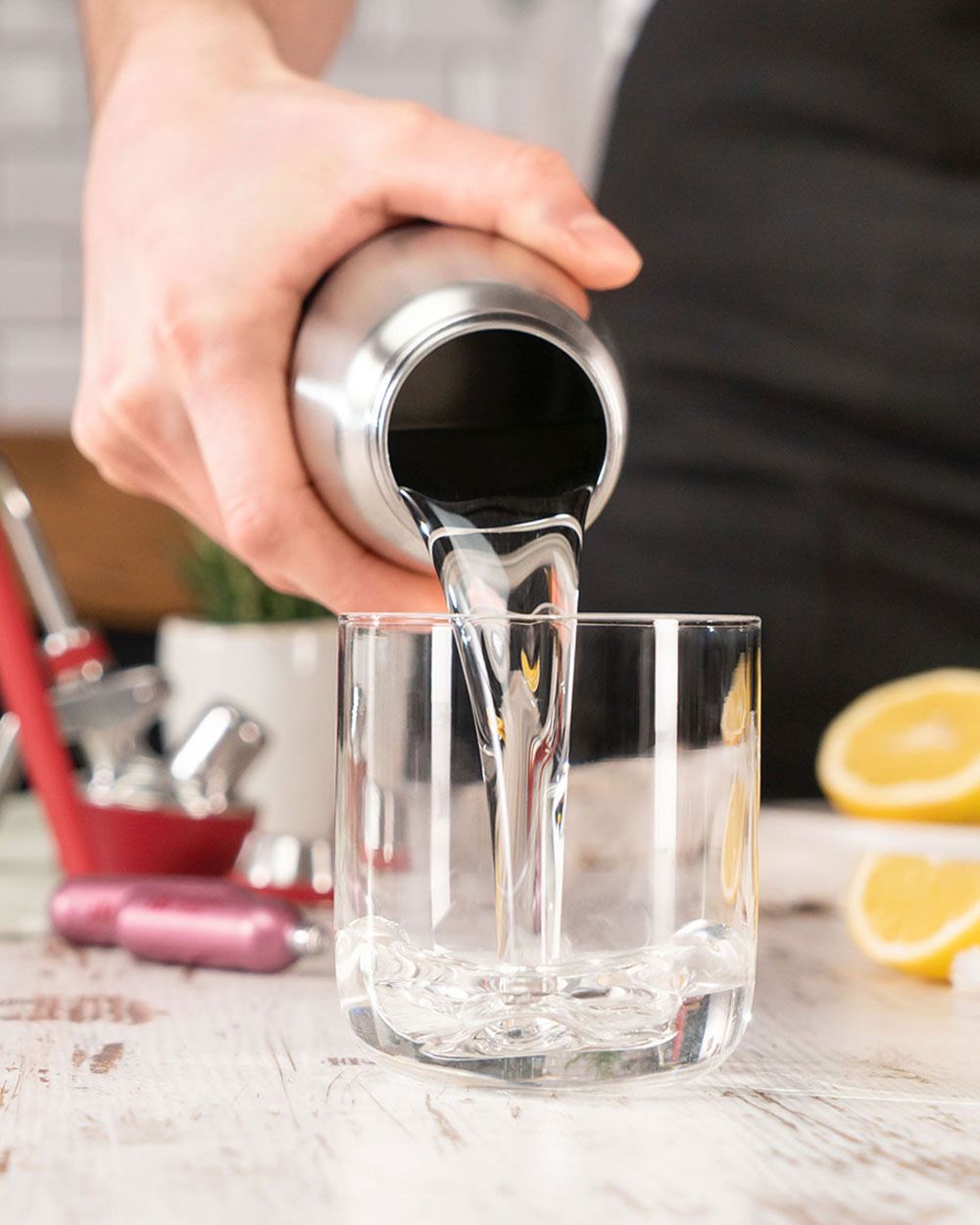 Jemand gießt Wasser in ein Glas, im Hintergrund ein iSi Gourmet Whip und iSi Charge Kapseln. 