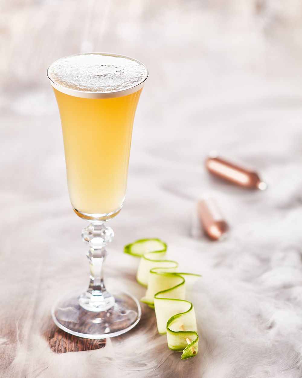 Ein Glas mit Nitro Red Bull Ginger Alle, daneben eine Gurkenspirale und zwei iSi Charge Kapseln. 