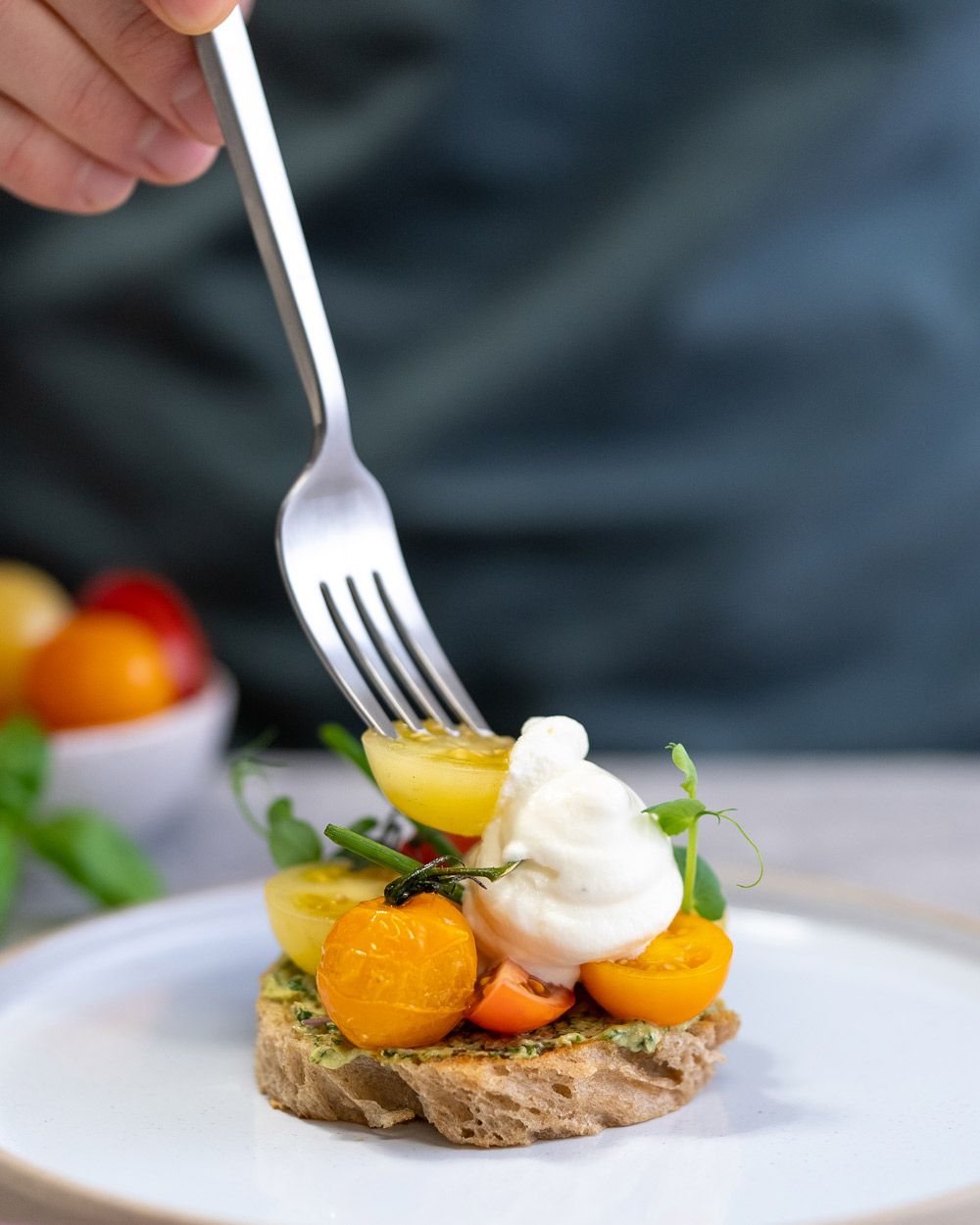 Jemand sticht mit einer Gabel  in ein Tomaten-Tarte mit Burrata Espuma. 