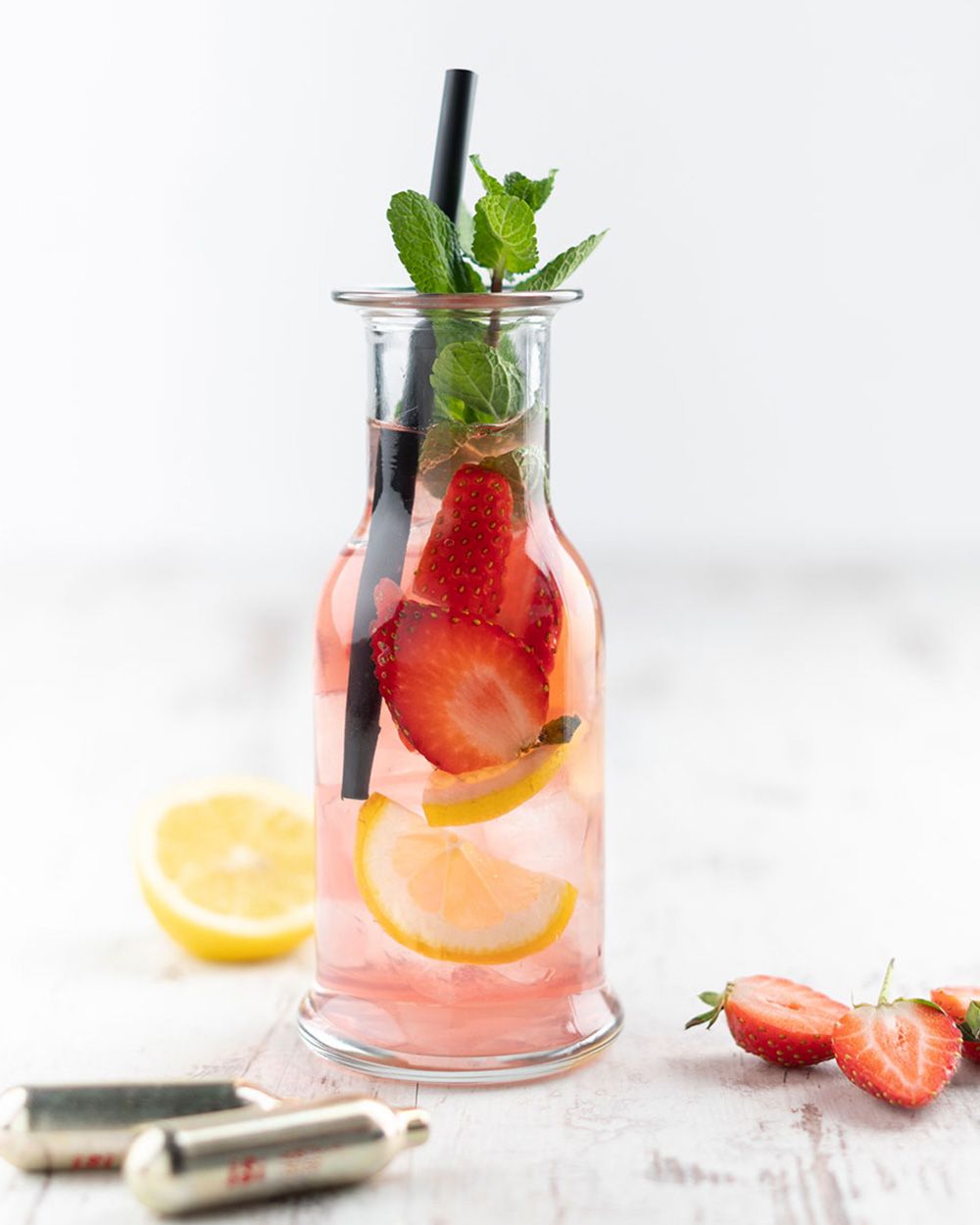 Ein großes Glas mit Limonade, Erdbeeren und Zitronen, daneben iSi Charge Kapseln. 