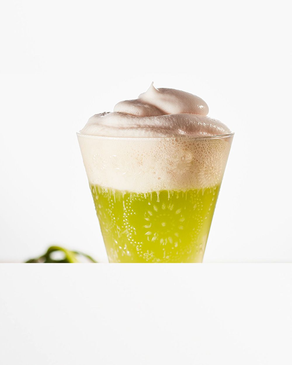 Auf dem Bild ist ein Glas mit grünem Getränk und einer Haube aus cremigem Schaum zu sehen.