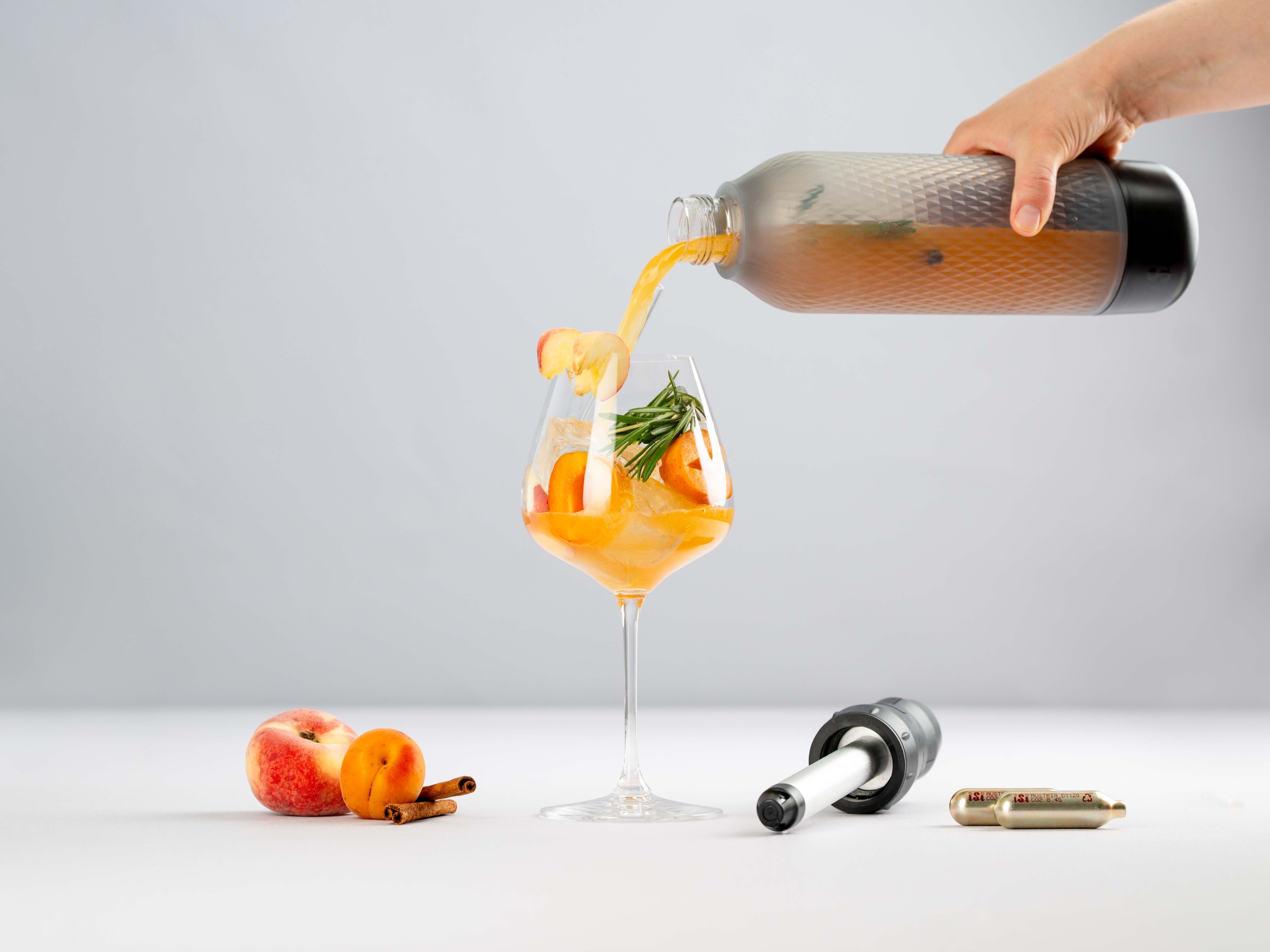 Jemand gießt aus einem iSi Twist'n Sparkle einen Apricot Spritz in ein Glas, daneben Marillen ein Twist'n Sparkle Aufsatz und iSi Charge Kapseln. 