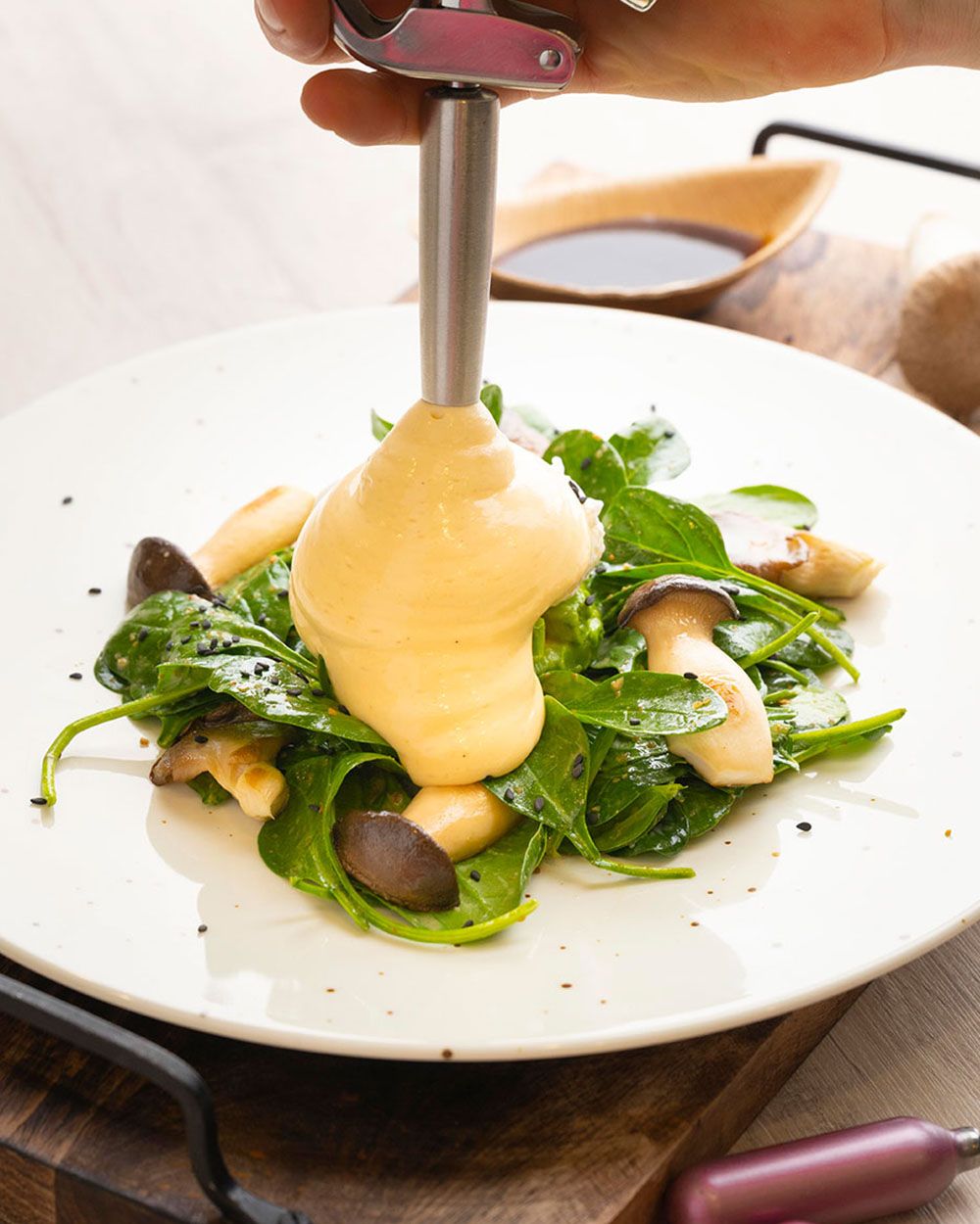 Jemand sprüht mit einer iSi Gourmet Whip Poke Sauce Hollandaise auf einen Salat. 