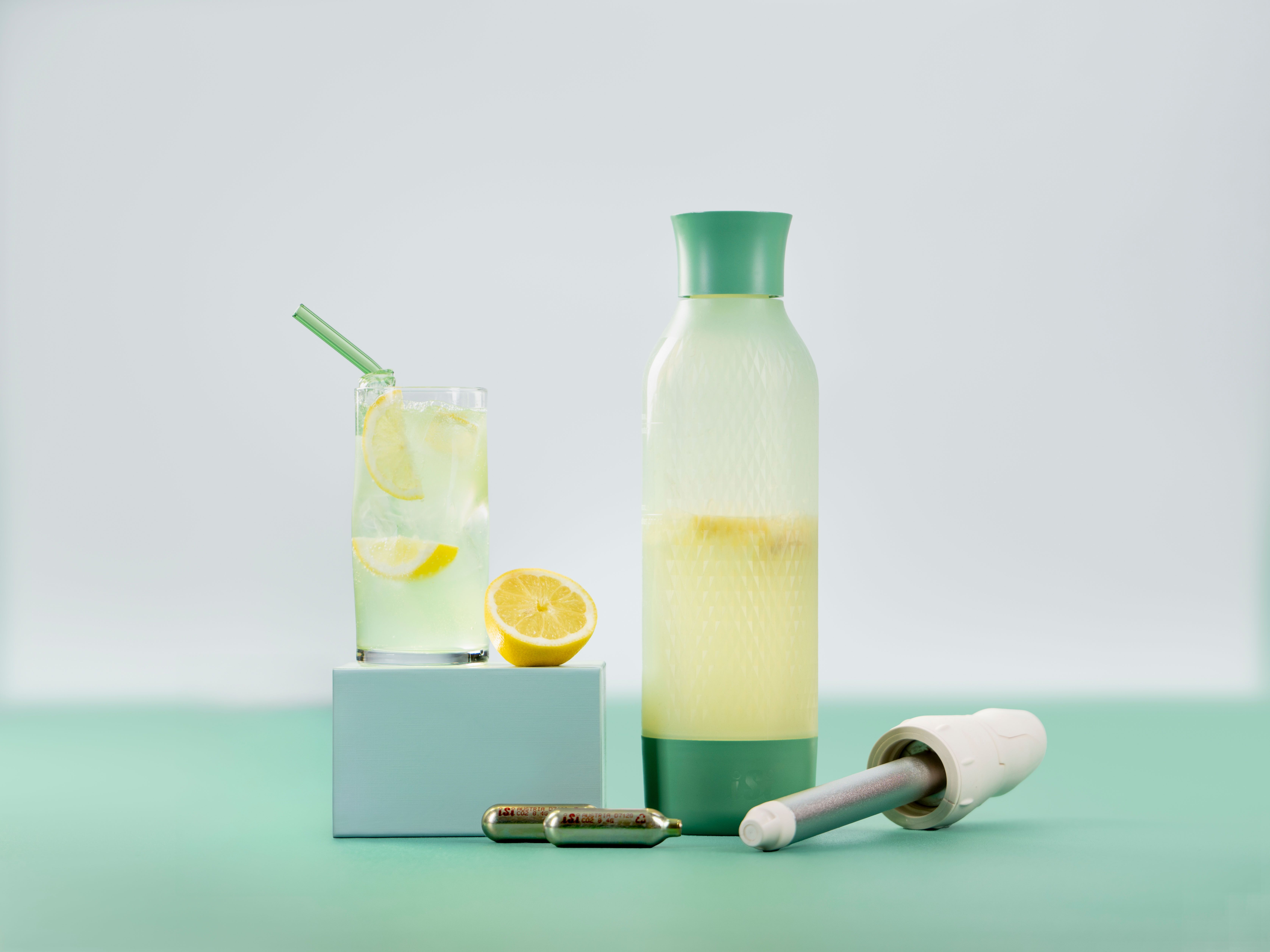 Ein Glas mit Ingwerlimonade, daneben eine Zitrone, iSi Charge Kapseln und ein iSi Twist'n Sparkle.