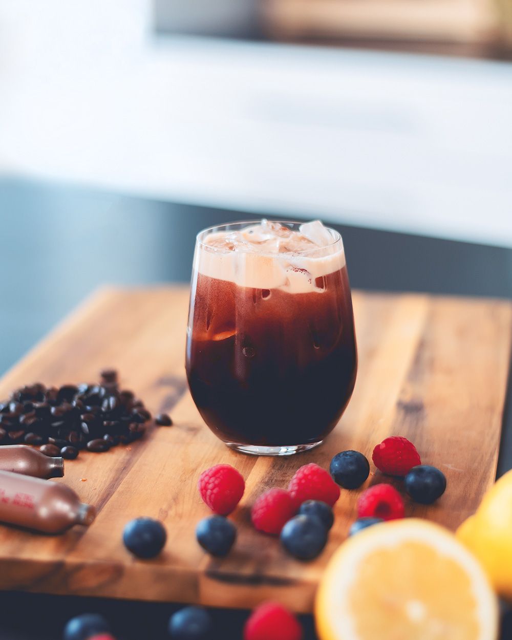 Ein Glas mit Bramble, daneben Beeren, Zitronen und iSi Charge Kapseln. 