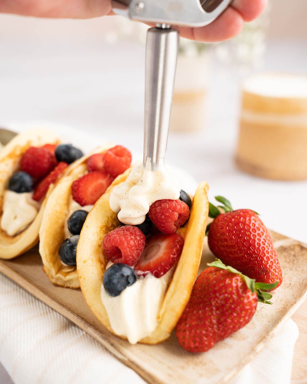 Jemand sprüht mit einen iSi Gourmet Whip Vanille-Mascarpone-Creme in einen Dessert-Taco mit Beeren. 