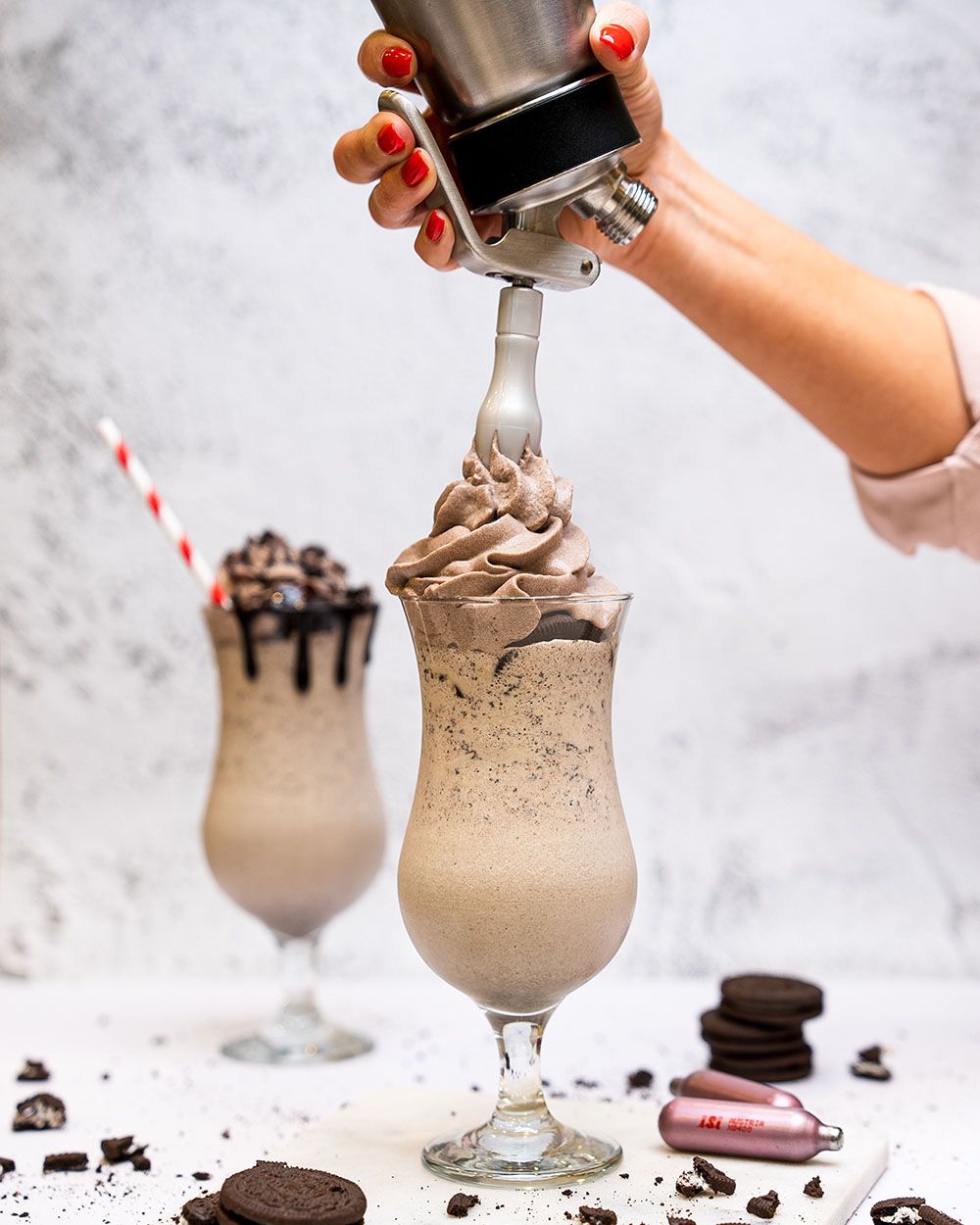 Jemand sprüht mit einem iSi Gourmet Whip Schaum auf einen Oreo Cafe Latte, daneben iSi Charge Kapseln und Oreo Kekse. 