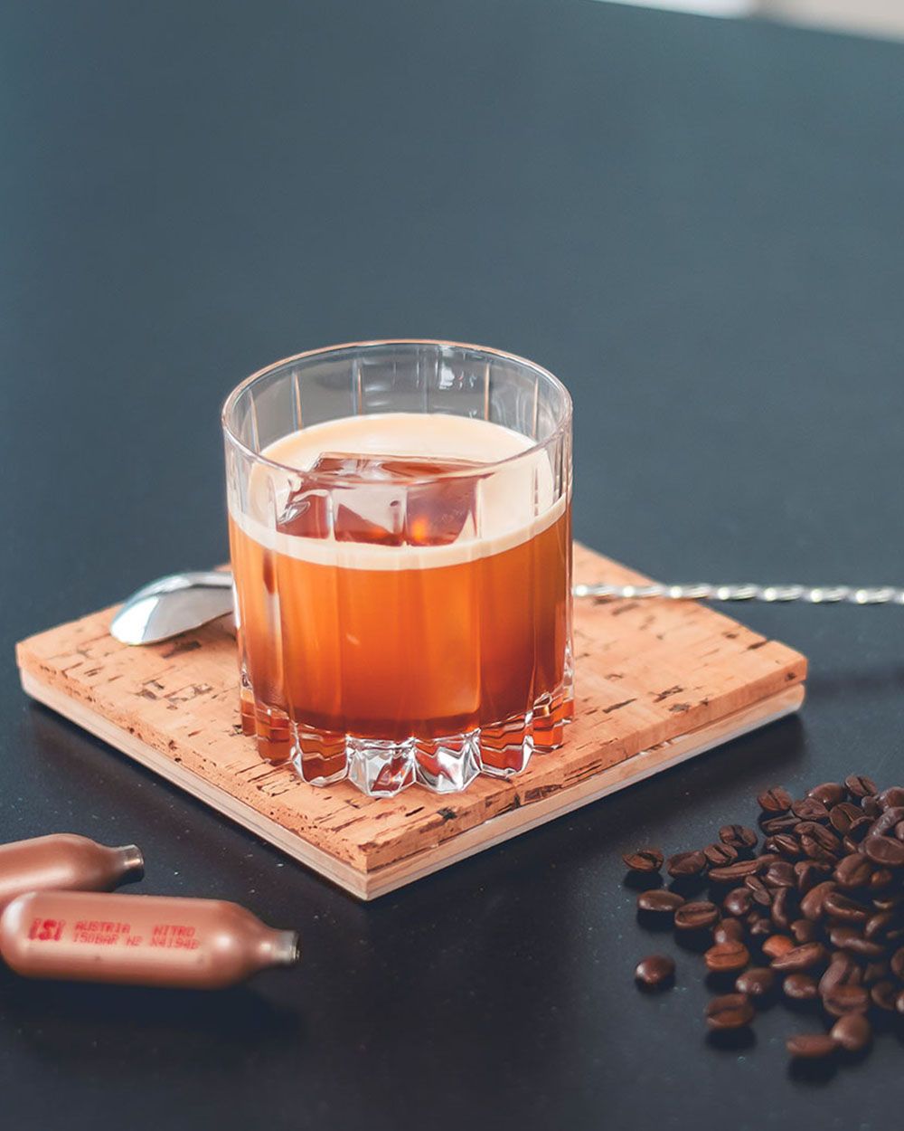 Ein Glas mit Nitro Whisky, daneben ein Löffel, Kaffeebohnen und iSi Charge Kapseln.
