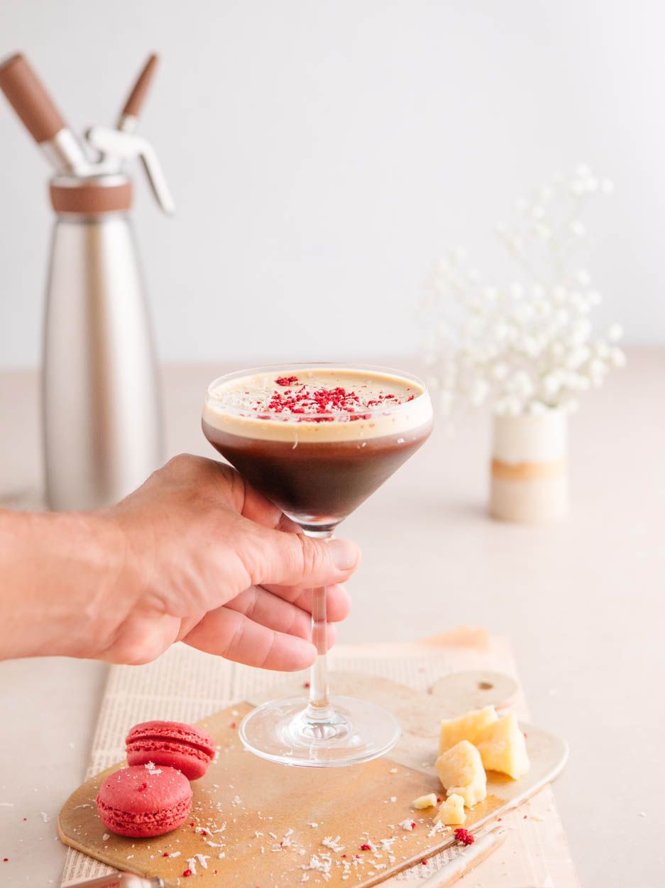 Jemand hält ein Glas Nitro Espresso Martini, daneben Macarons und im Hintergrund ein iSi Nitro. 