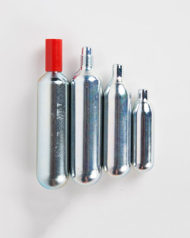 Vier verschieden große N2O Kapseln, eine davon mit einer roten Kapsel