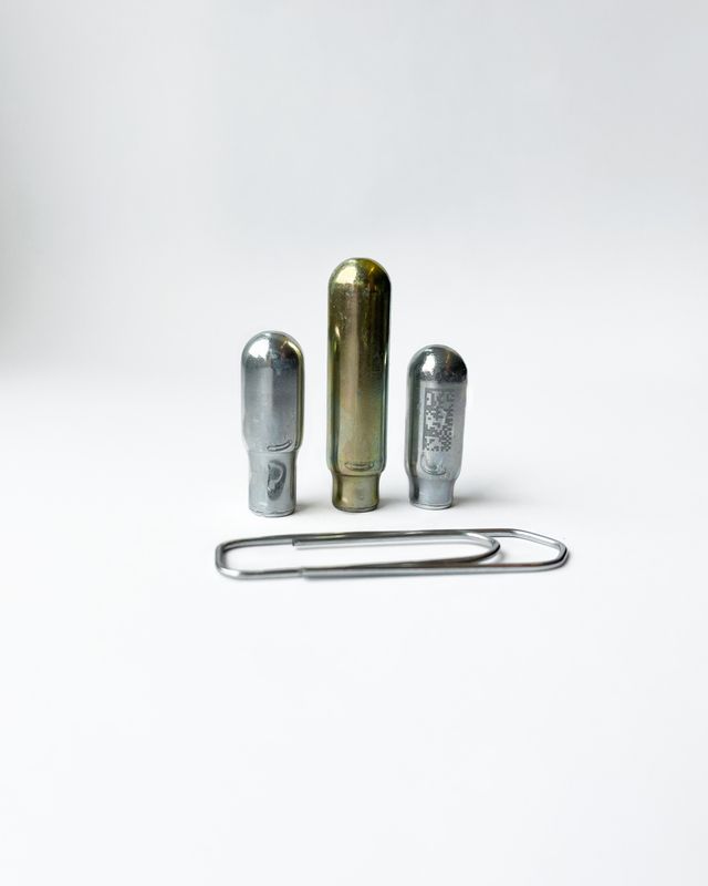 Drei kleine Gaskapseln mit einer Büroklammer davor zum Größenvergleich