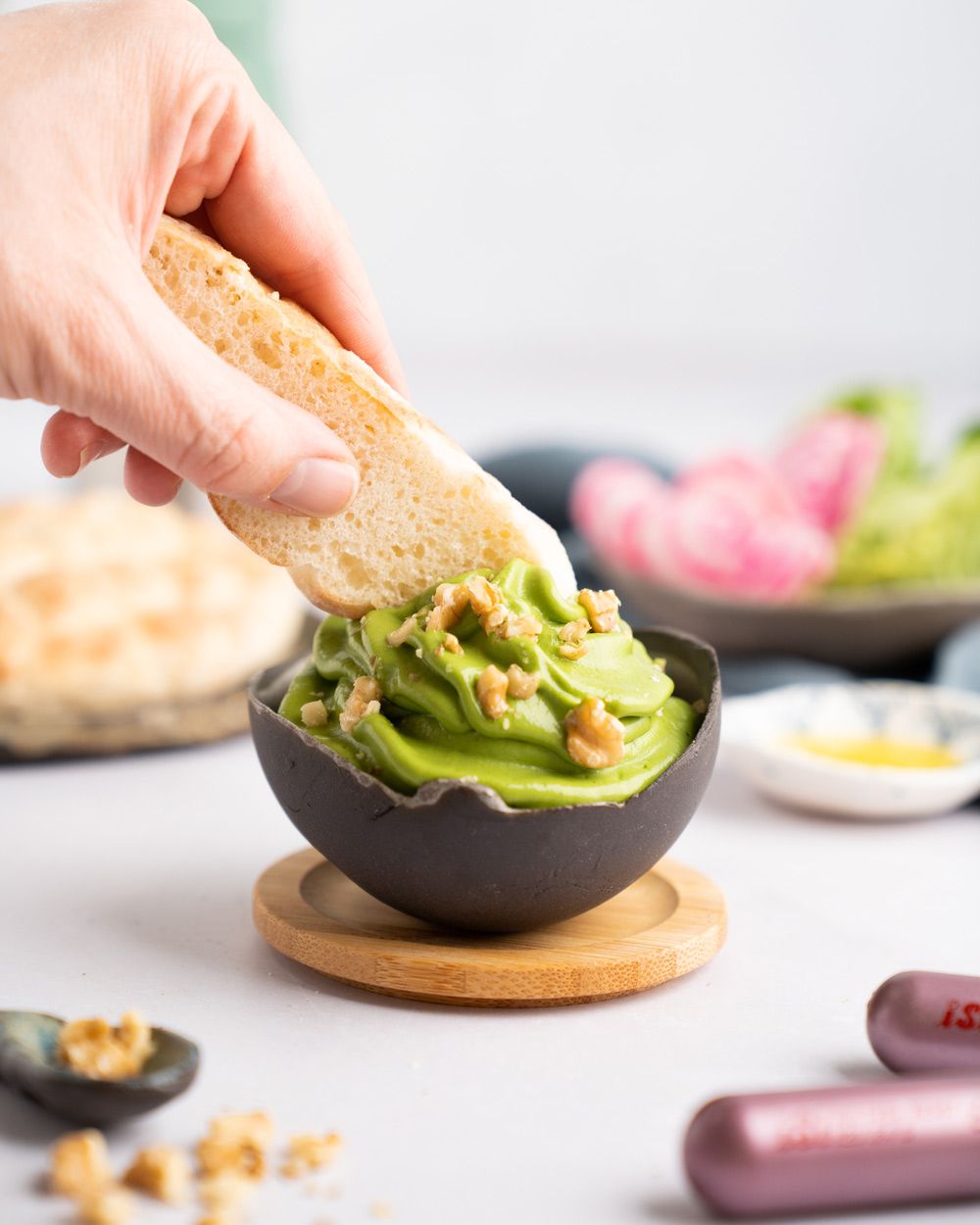 Jemand taucht Pita-Brot in eine Schüssel mit Green Goddess Dip. Im Hintergrund sind Zutaten zu sehen, im Vordergrund zwei iSi Charge Kapseln. 