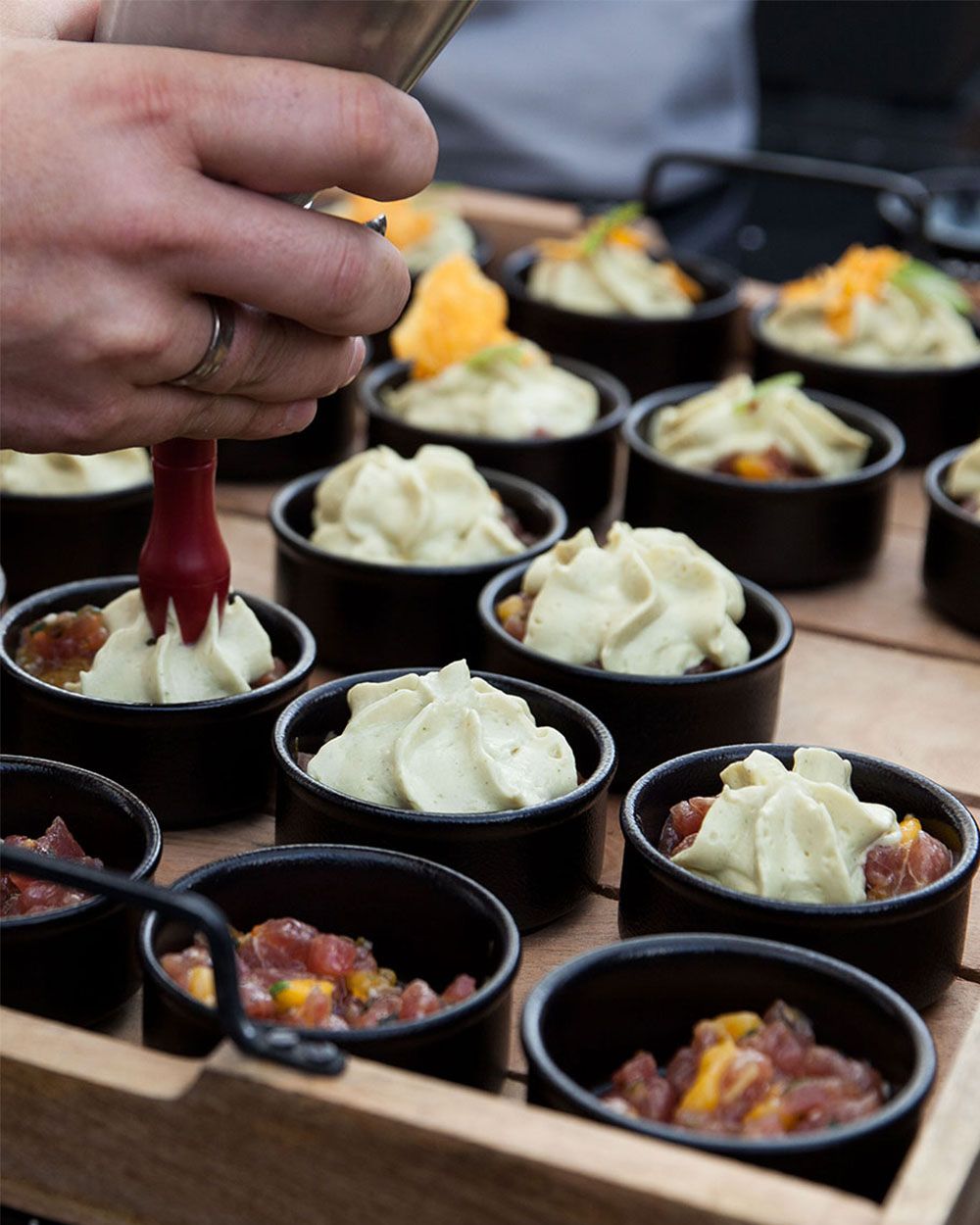 Jemand sprüht mit einem iSi Gourmet Whip Schaum in eine Schüssel mit Thunfisch-Tartar, daneben viele weitere Schüsseln. 