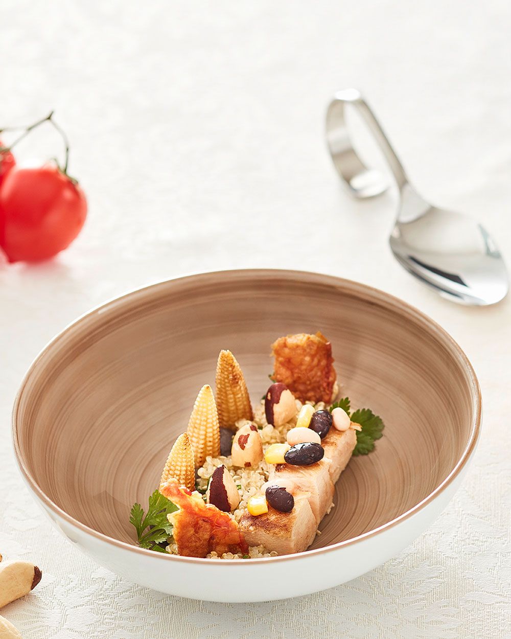 Ein Teller mit Pollo, Quinoa und Bohnen, daneben ein großer Löffel und Tomaten.