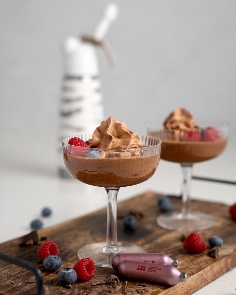 Zwei Gläser mit veganem Schokomousse, daneben frische Beeren und iSi Charge Kapseln, im Hintergrund ein iSi Creative Whip. 