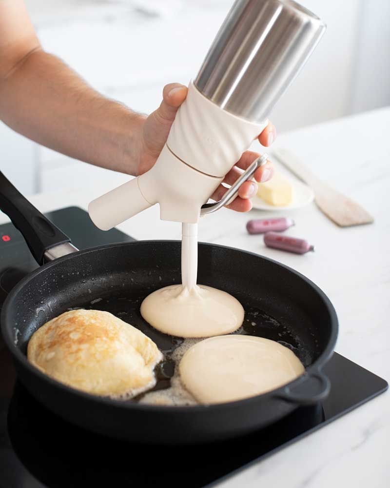 Jemand sprüht mit einem iSi Creative Whip Pancake Masse in eine Pfanne, daneben iSi Charge Kapseln. 