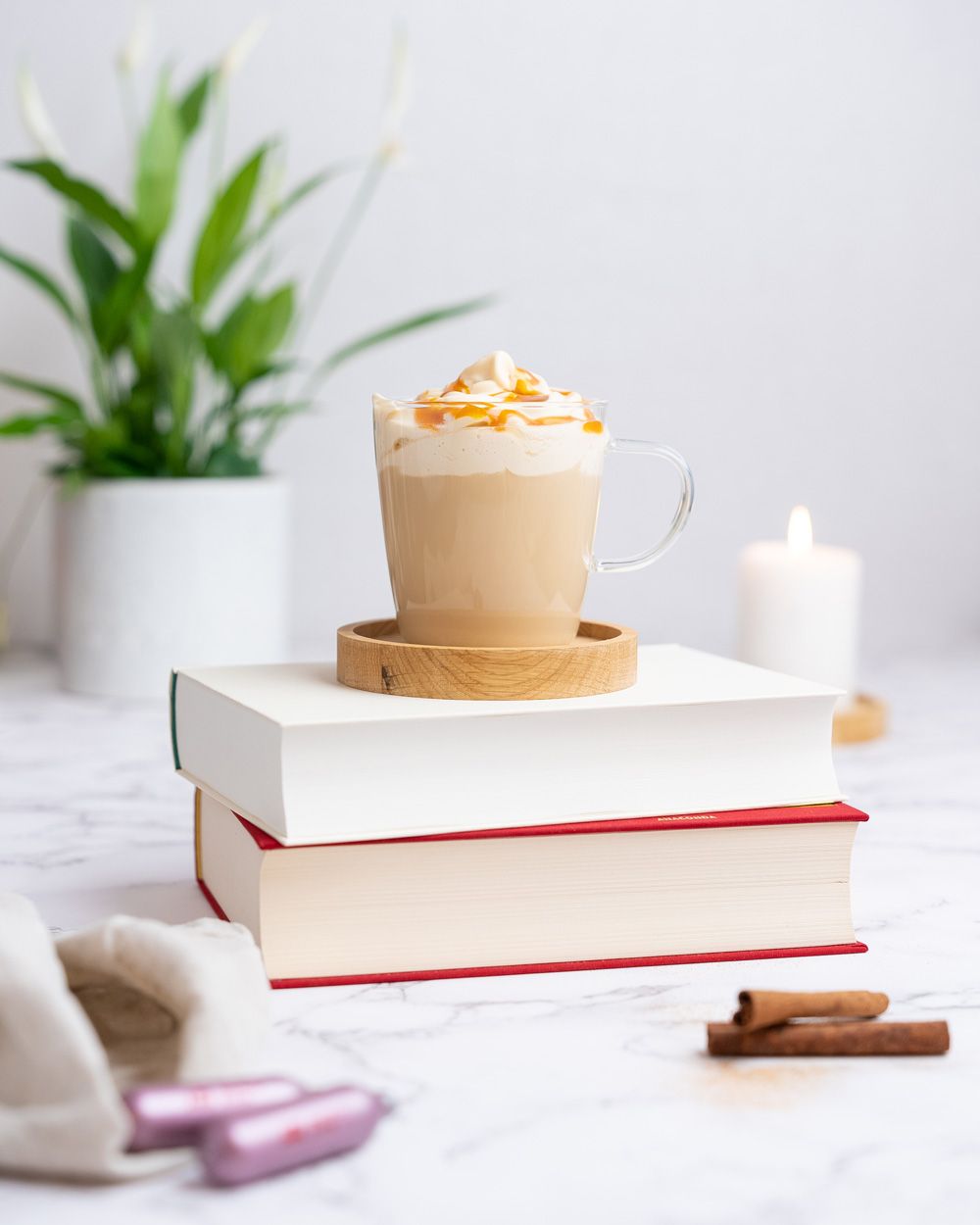 Auf einem Stapel Bücher steht ein Glas mit einem Kaffeegetränk mit Salted Caramel, davor Zimtstangen und iSi Charge Kapseln.